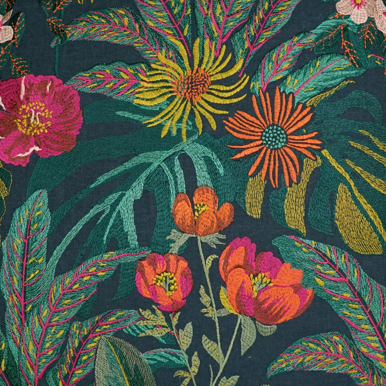 Vibrant tropical floral fabric with pink, orange and yellow blossoms and green leaves on a dark teal background.