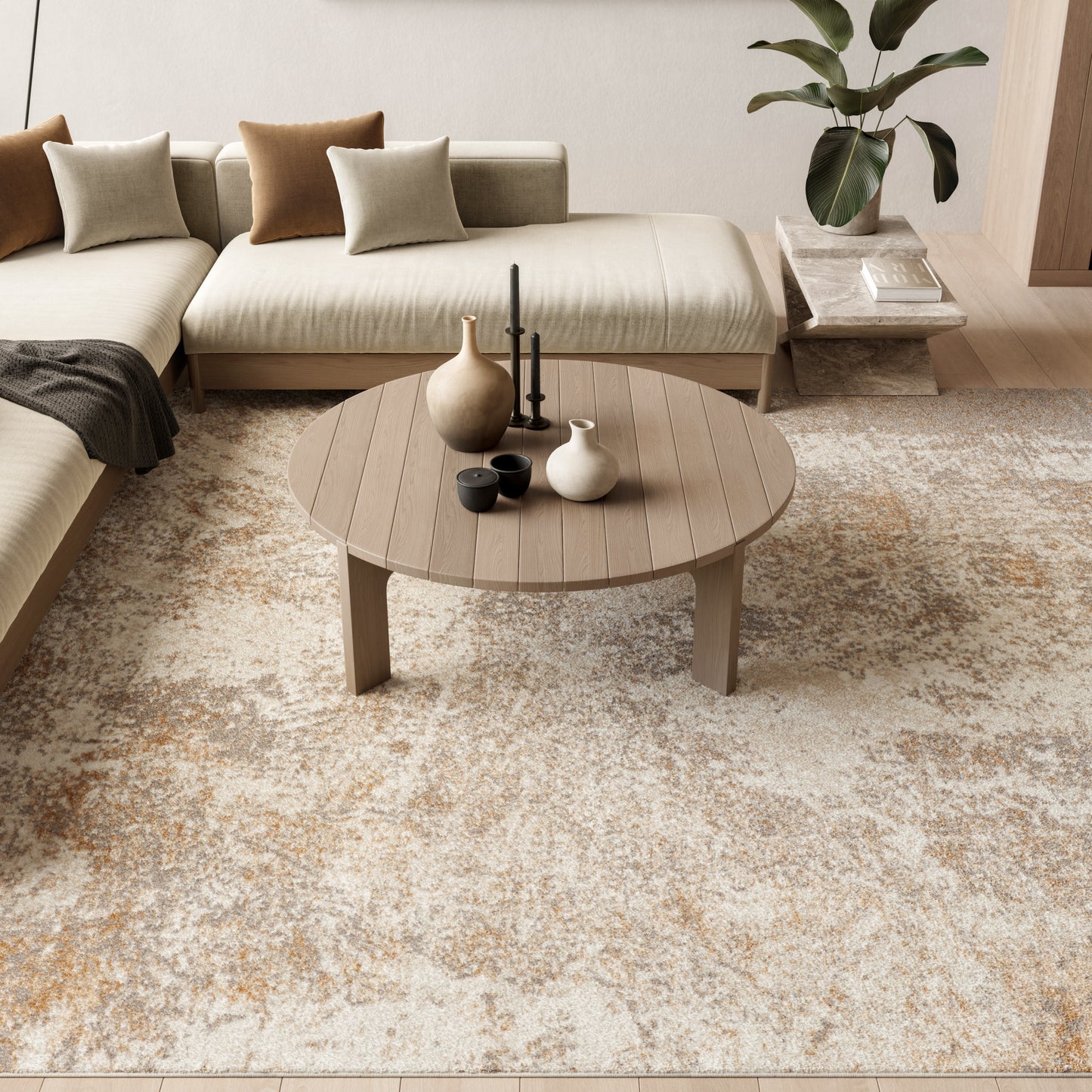 Modern 8' x 10' beige rug in a living room with a round wooden coffee table, vases on the table, a beige sectional sofa with neutral cushions, and a plant.