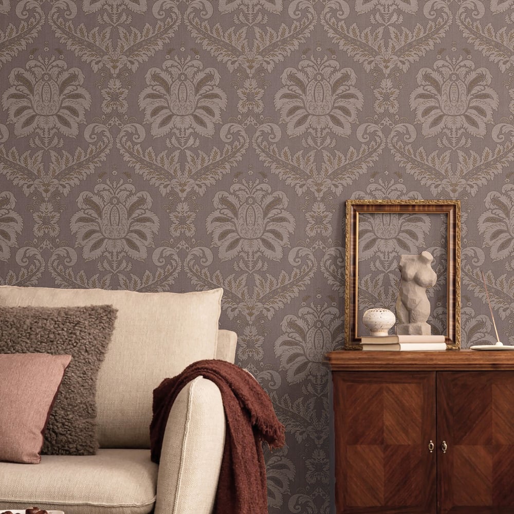 Damask purple and gold textured wallpaper behind a beige sofa with pink/brown cushions and a burgundy throw; wooden cabinet with a framed statue.