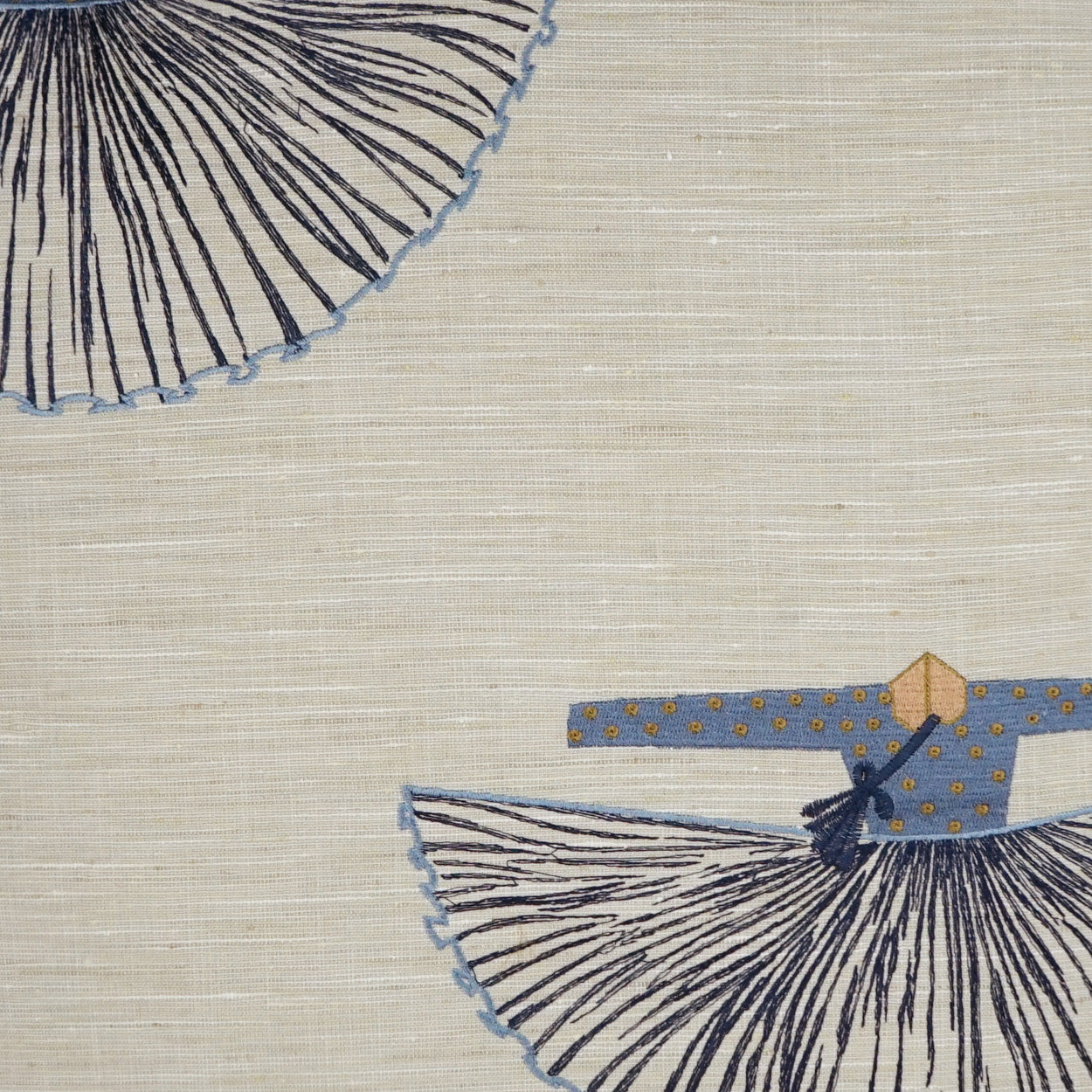Beige linen with navy radiating circular embroidery and a blue stripe with yellow dots, plus a small blue-yellow figure.
