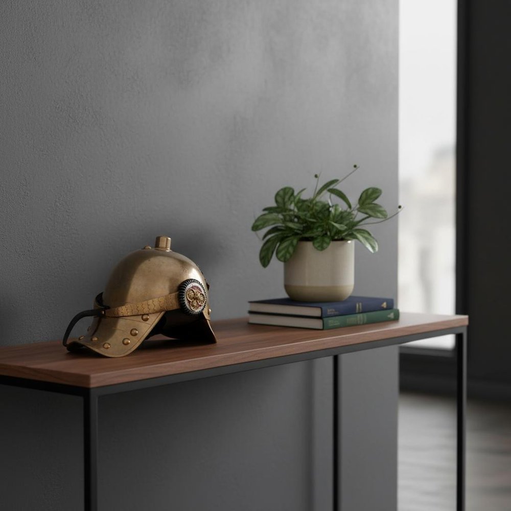 Brass steampunk helmet on a wooden console table beside a leafy potted plant and a stack of books.