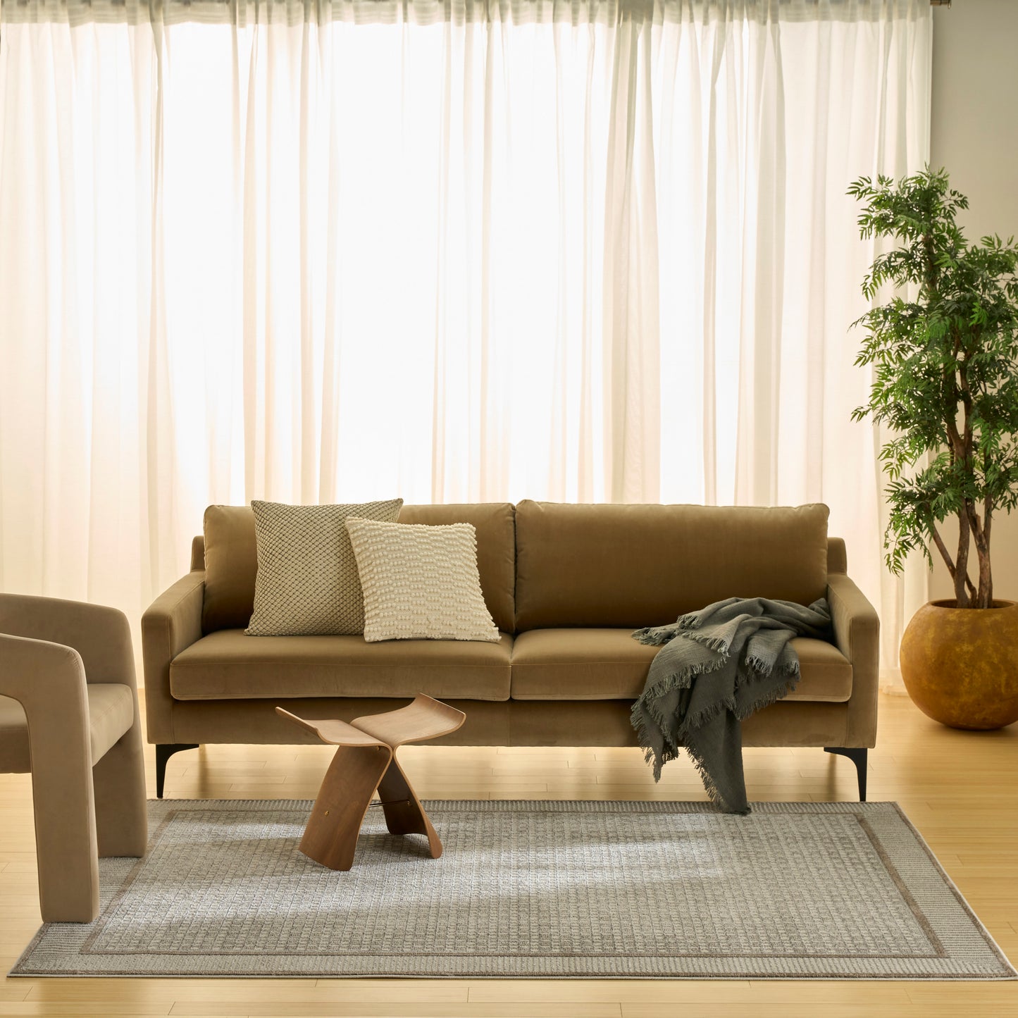 Beige fabric sofa with two textured cushions, gray throw, sculptural wood coffee table, light gray rug and potted plant.