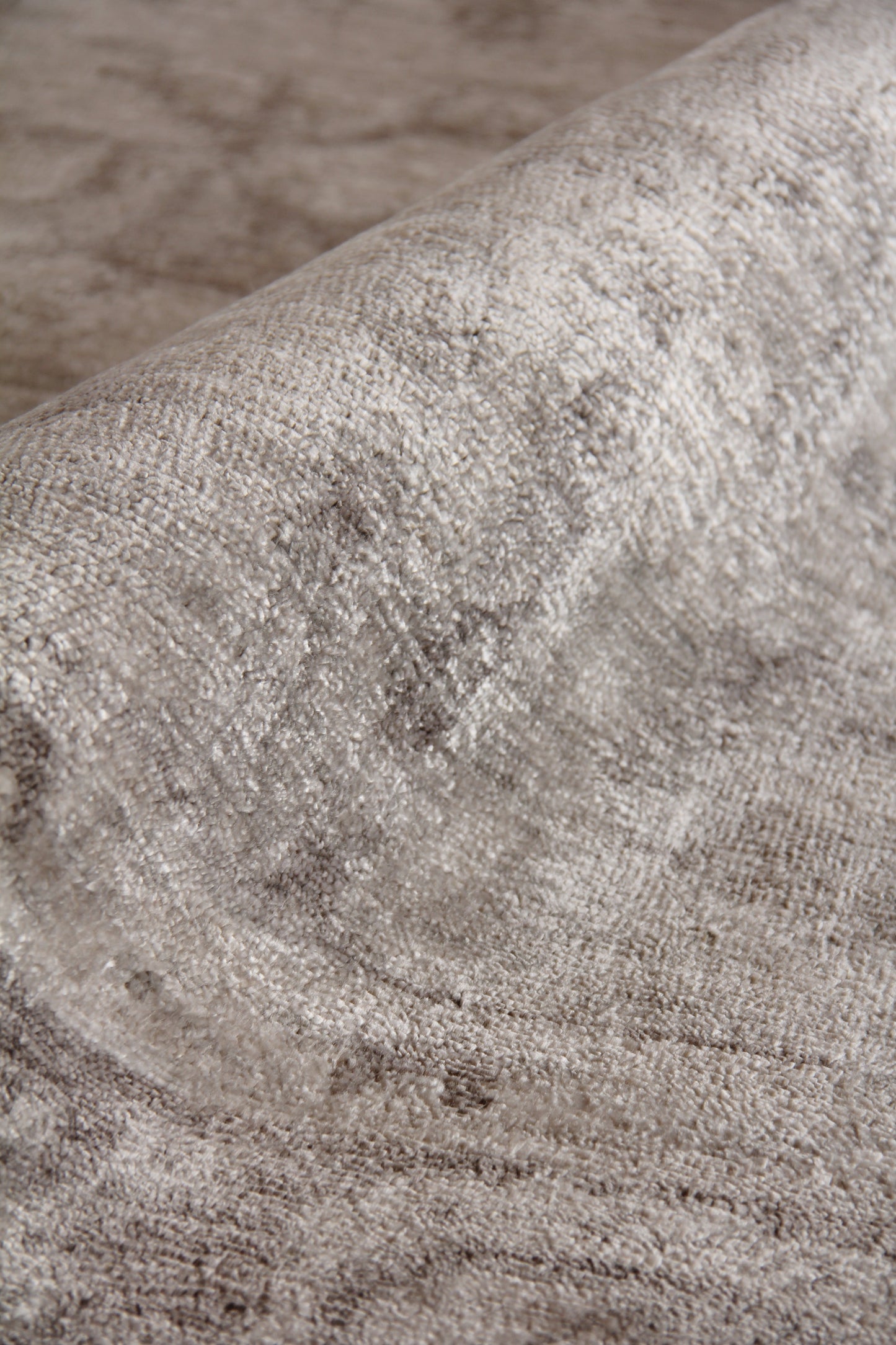 Beige textured area rug with dense plush pile and rolled edge, neutral taupe tones.