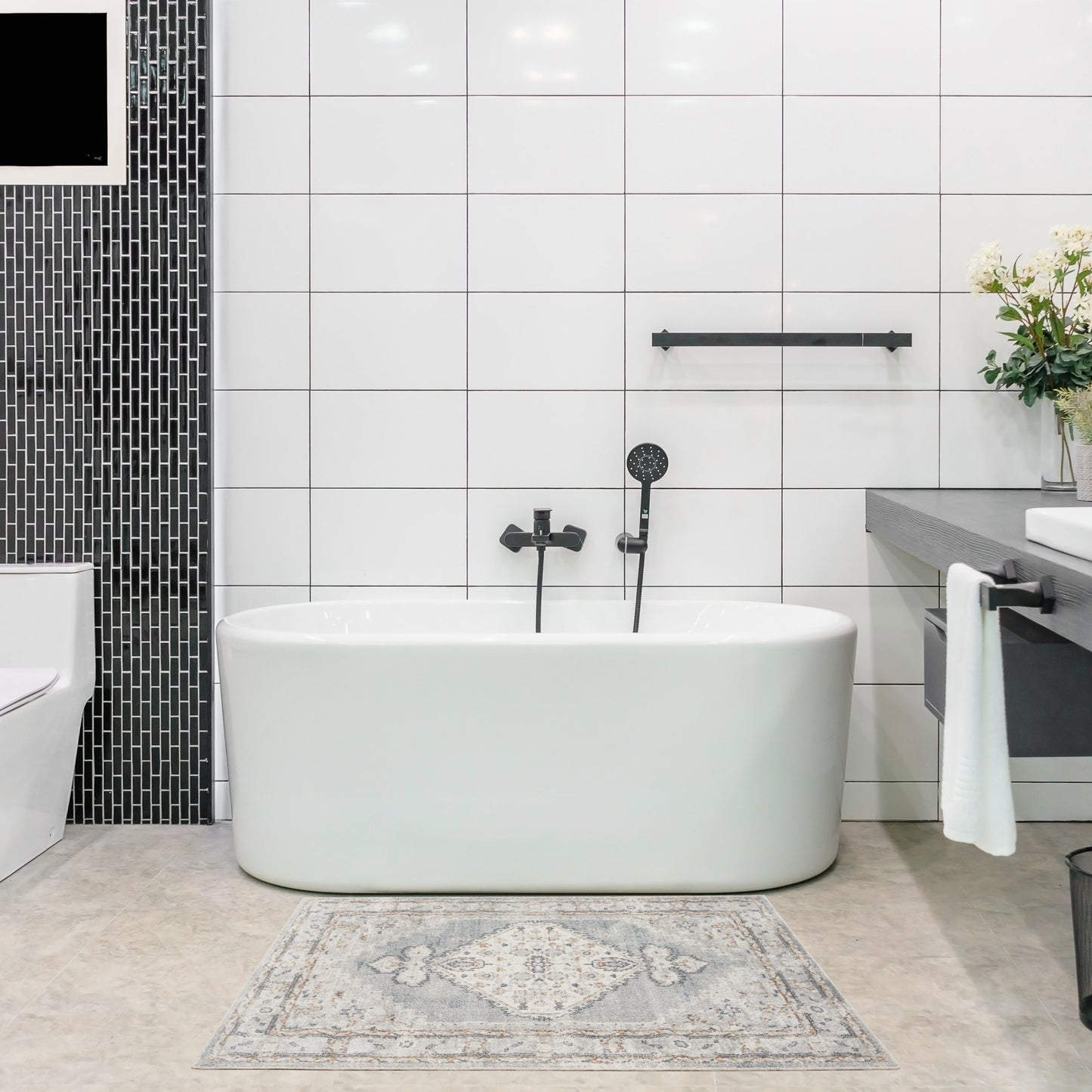 White freestanding oval bathtub with black fixtures in a modern tiled bathroom, featuring a black mosaic wall and vanity.