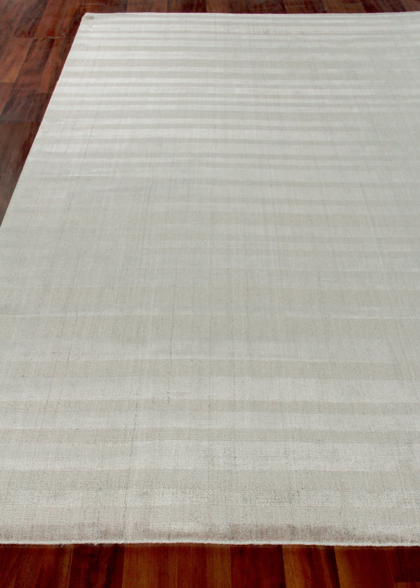 Ivory hand loomed rug with faint horizontal stripes, rectangular for contemporary living spaces on wood floors.