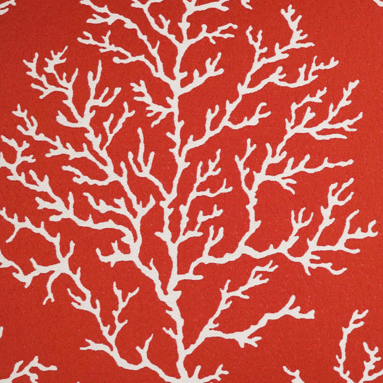 Orange-red pillow with a white coral-branch pattern; bold botanical design.