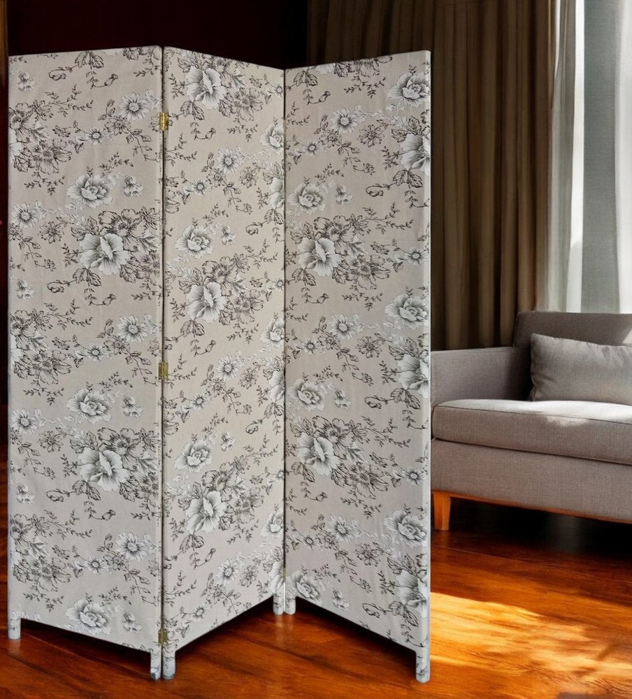 Three-panel decorative folding screen with light beige fabric and gray floral pattern, standing on wooden legs in a living room.