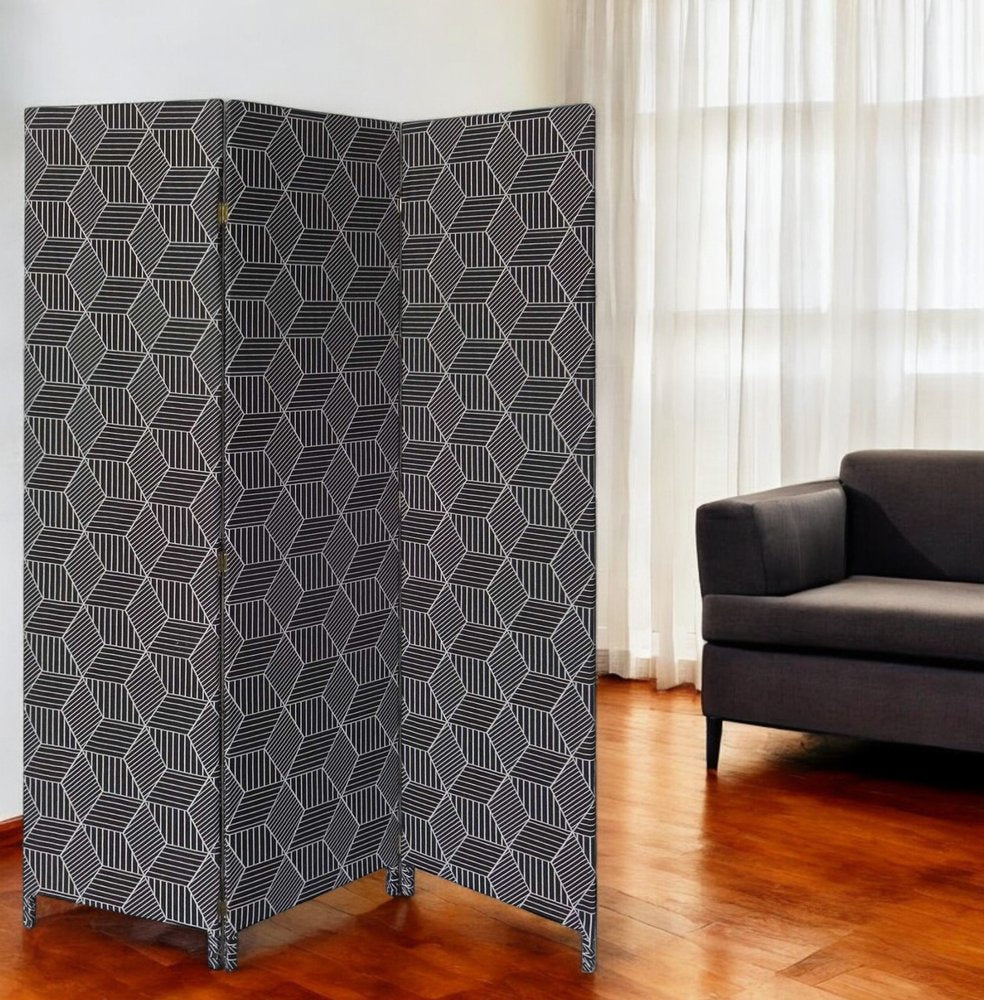 Three-panel folding screen in navy fabric with white geometric diamond pattern; stands on small feet by a gray sofa in a wooden-floored living room.