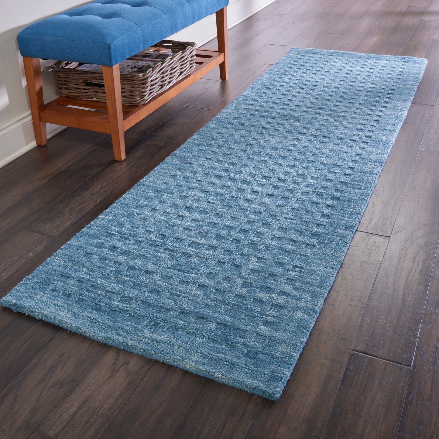 Blue textured hallway runner rug, 8' long, on dark wood floor beside a wooden bench with tufted blue cushion and wicker basket shelf.