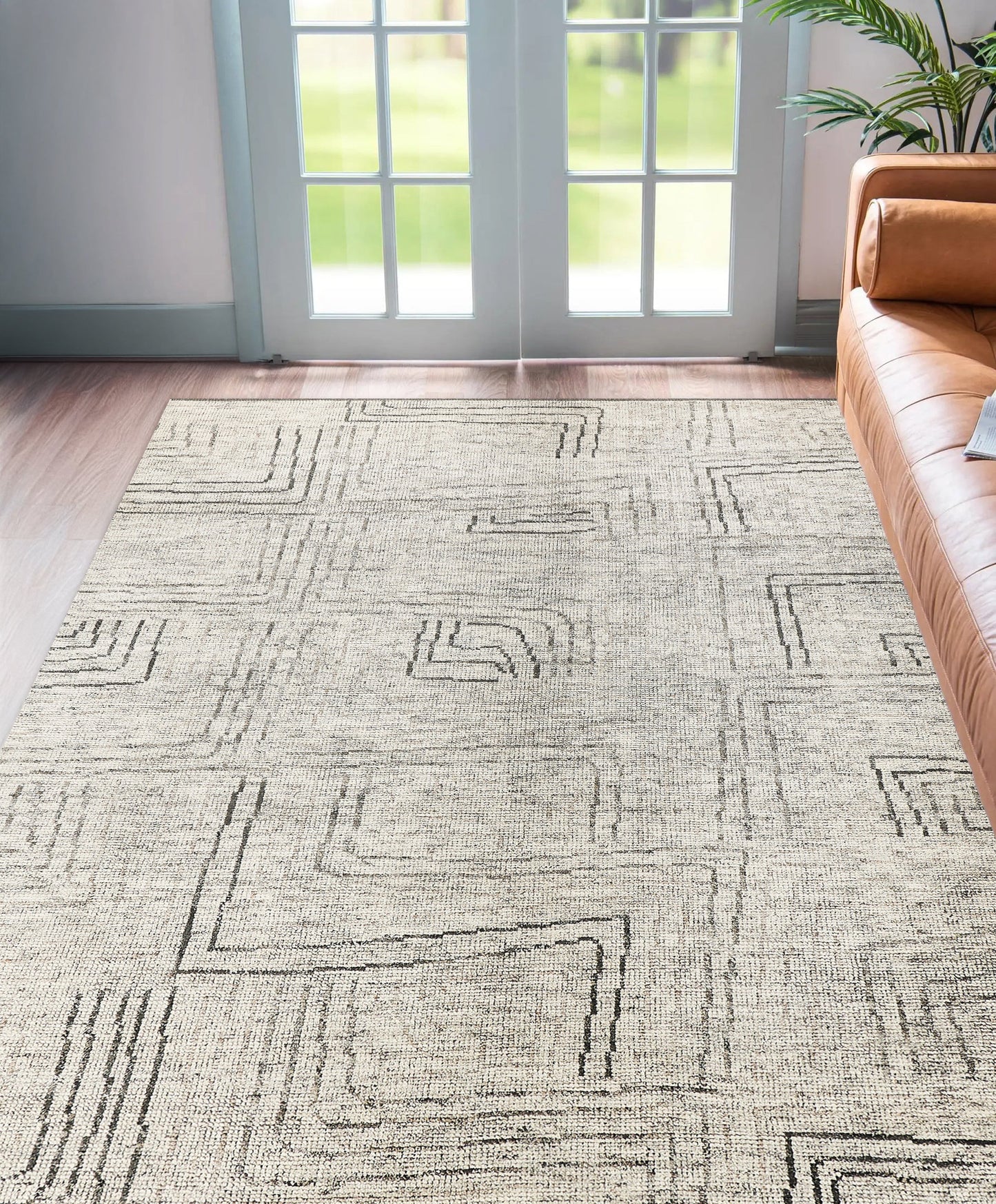 Light gray geometric area rug with black square-line patterns, in a living room with a brown leather sofa and French doors.