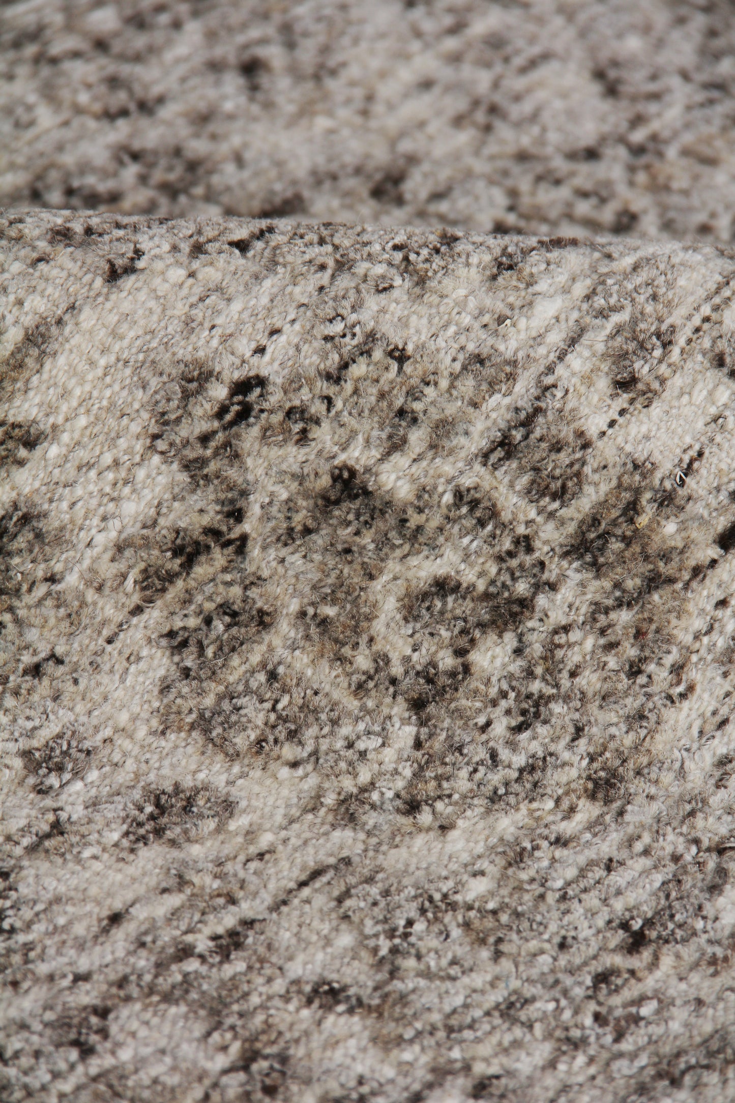 Close-up of beige-gray speckled hand-knotted rug fibers and textured pile.