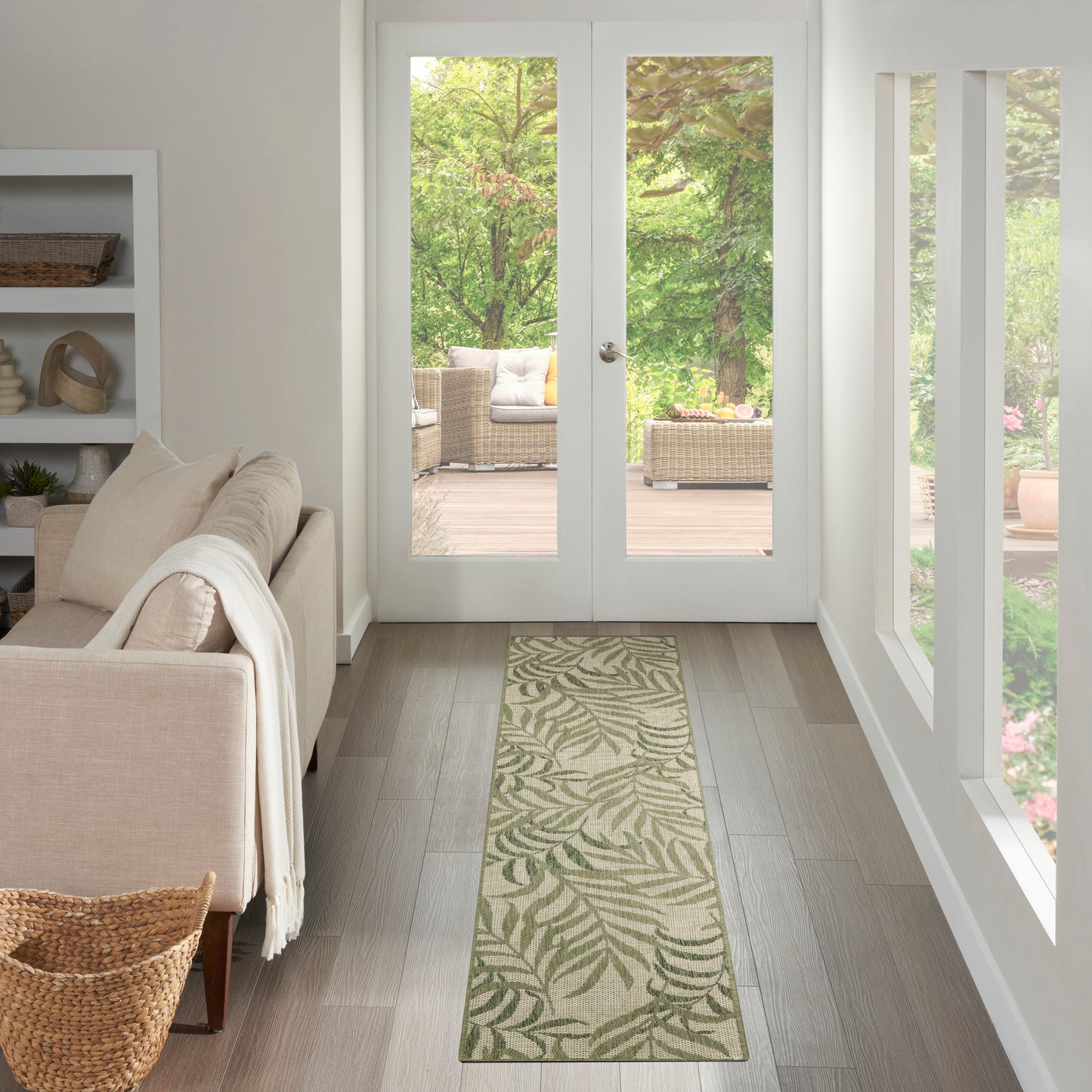 Beige long runner rug with green leafy botanical pattern in a bright living room with glass doors to a garden.