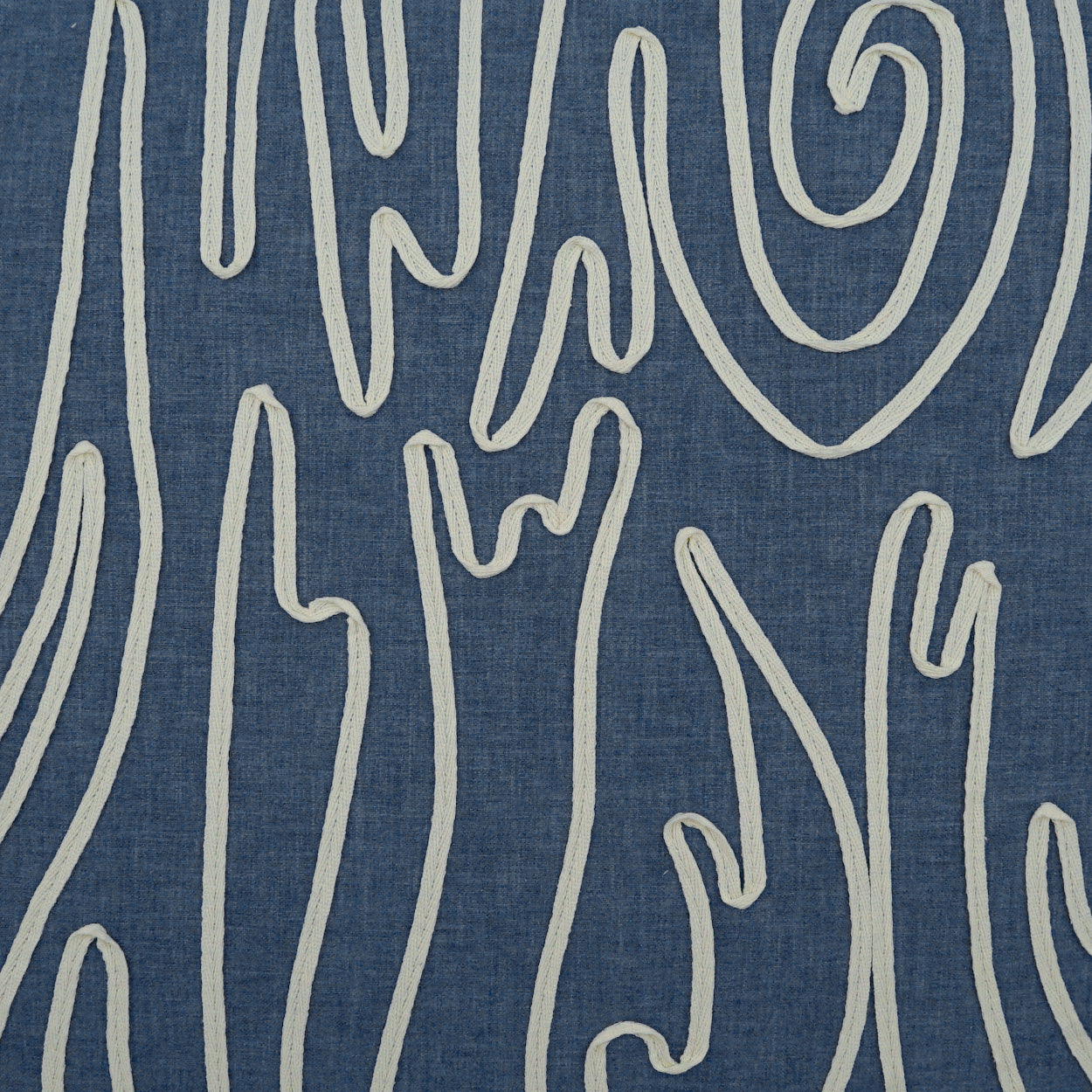 Blue fabric with white abstract squiggle lines; cord-like doodle pattern for upholstery or apparel.