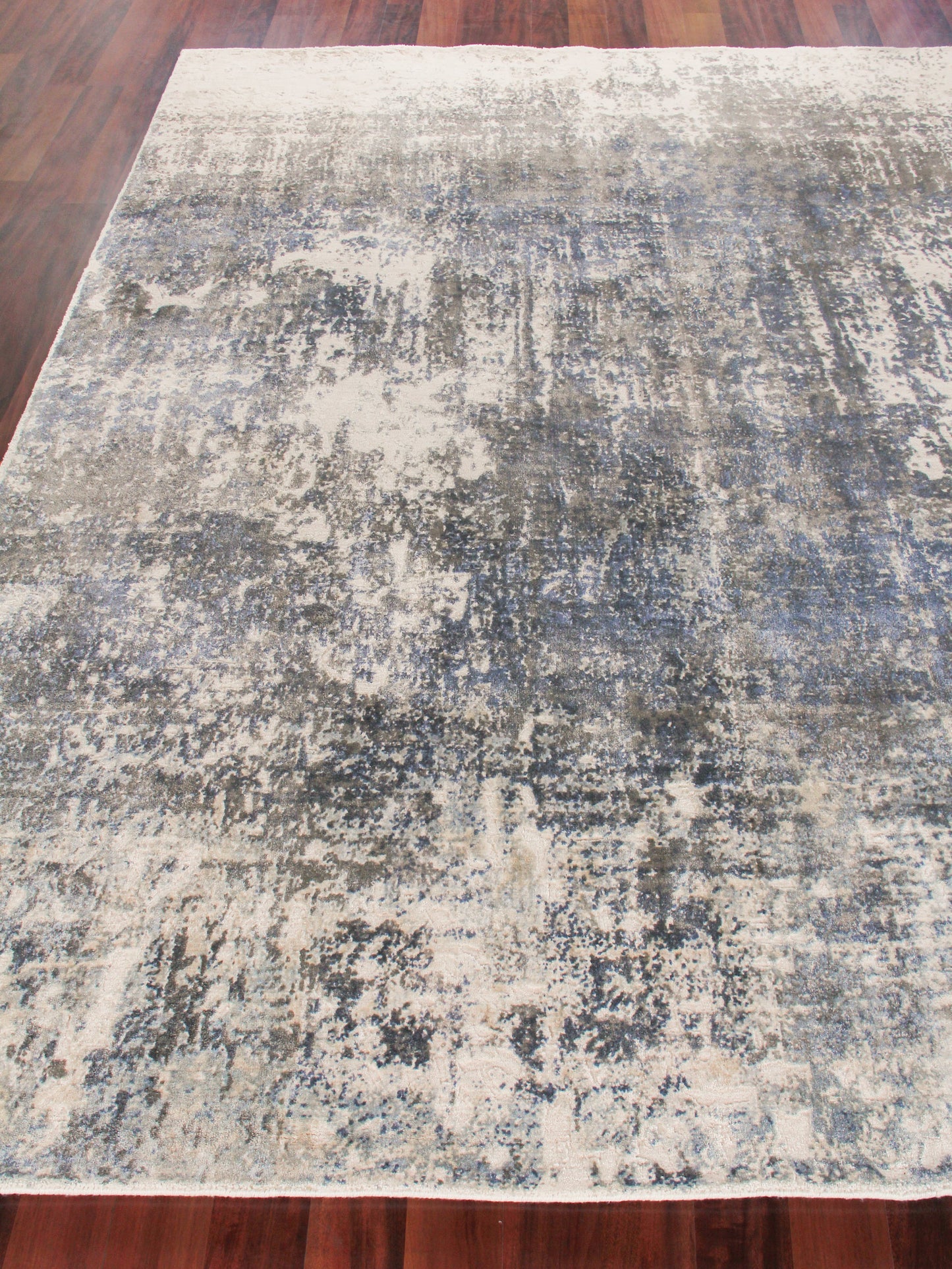 Abstract distressed area rug in blue, gray and ivory on a wooden floor; modern, plush texture.