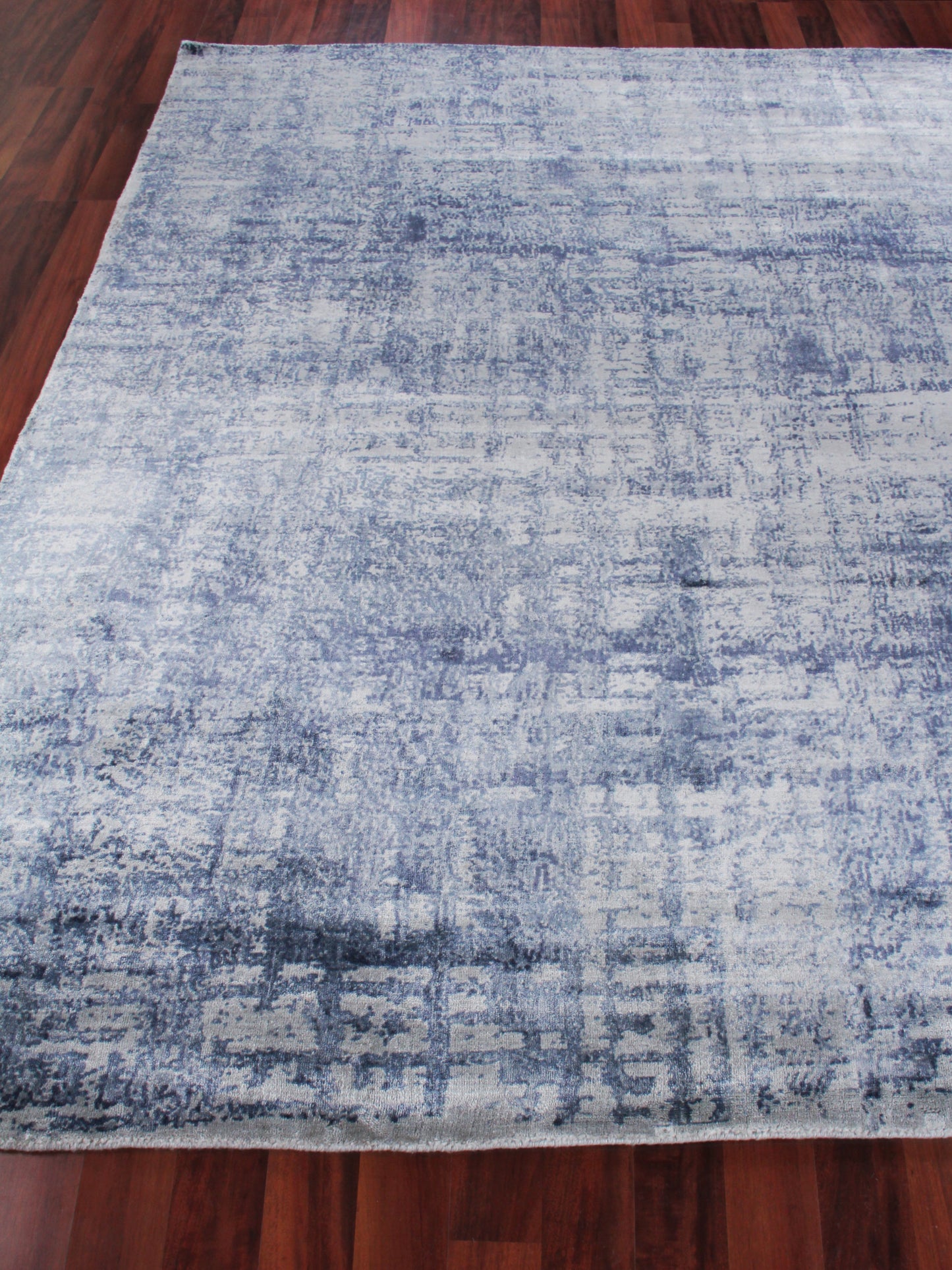 Blue-gray distressed area rug with abstract pattern on dark wood floor; rectangular.