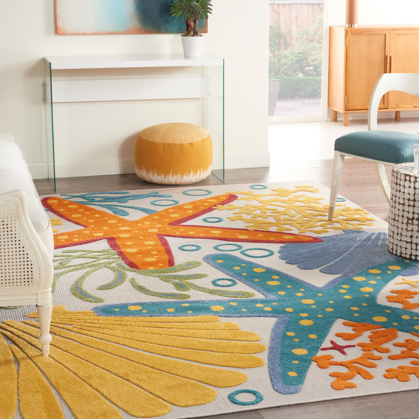 Rectangular coastal area rug featuring bright yellow starfish, teal blue seaweed and orange accents in a bright living room.