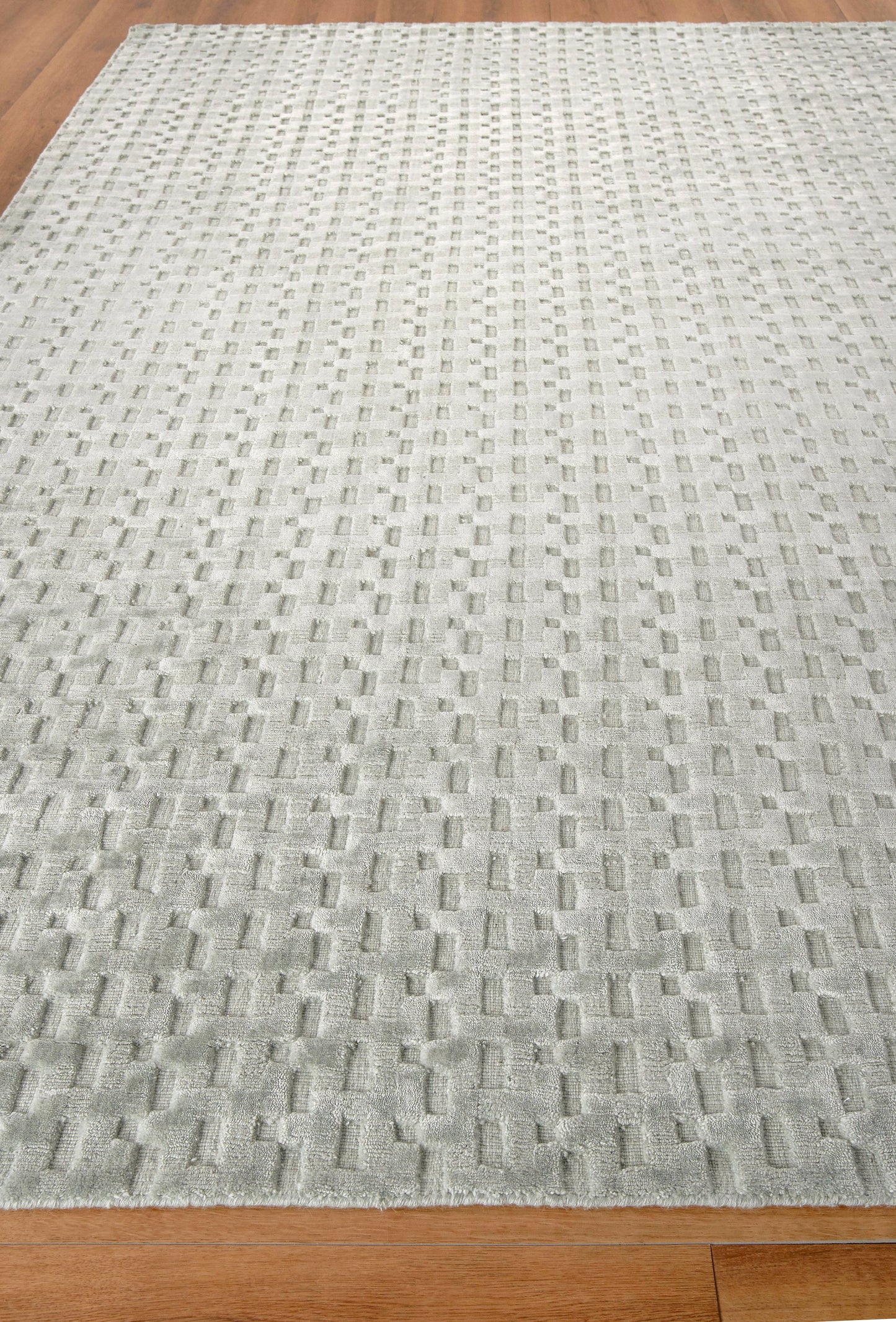 Light gray textured area rug with a grid of raised rectangular blocks on a hardwood floor.