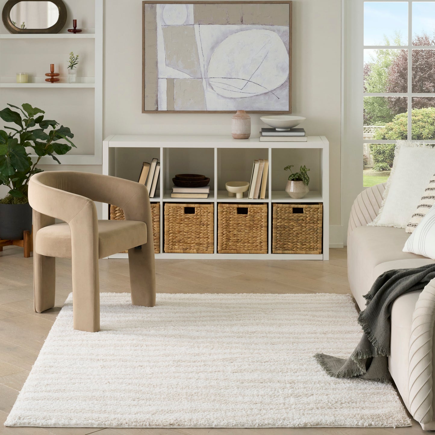 Cream shag rug in a light beige room with a curved beige chair, white cubby storage, woven baskets, and abstract wall art.