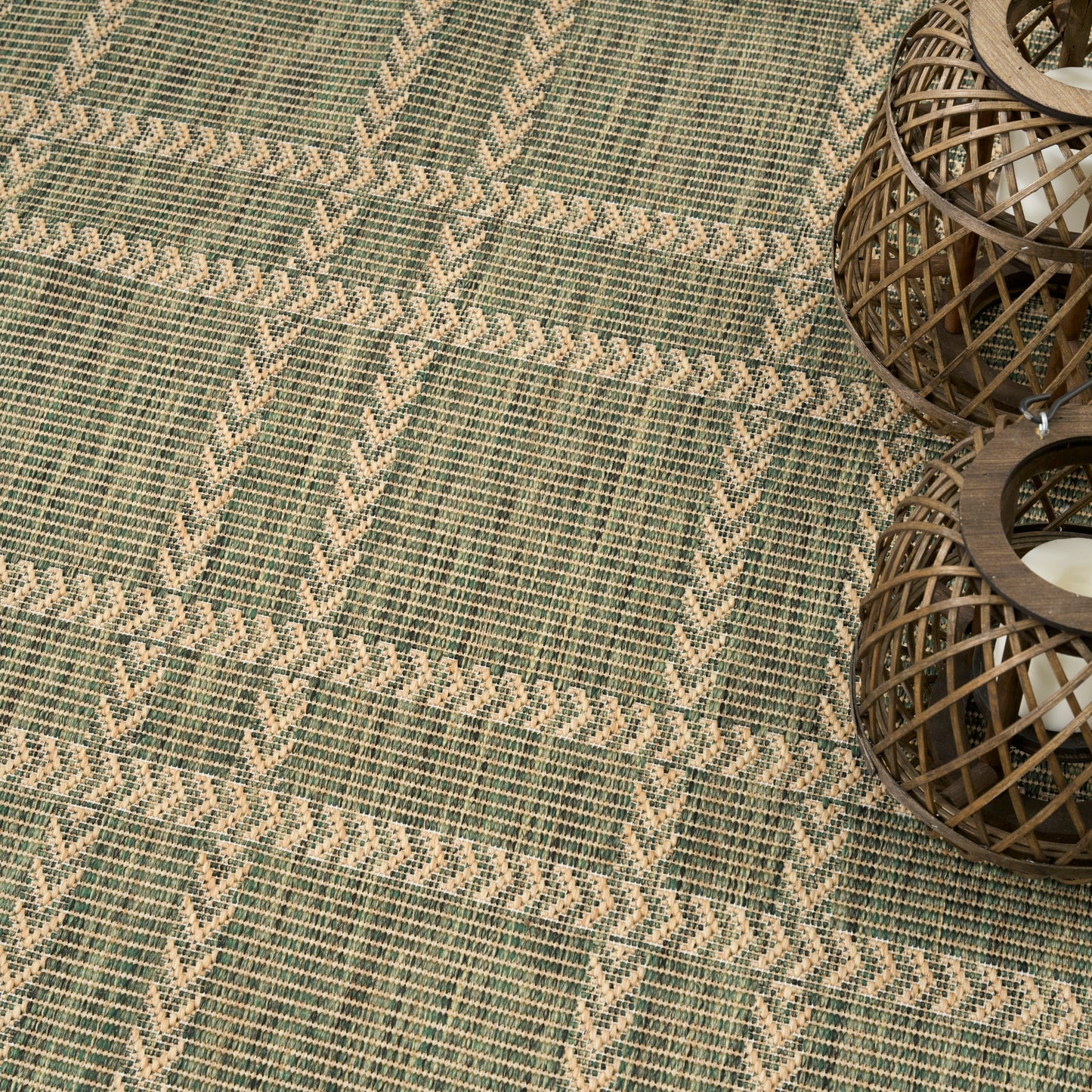 Woven green and beige rug with diagonal chevron lattice pattern and two brown wicker lanterns on the right.