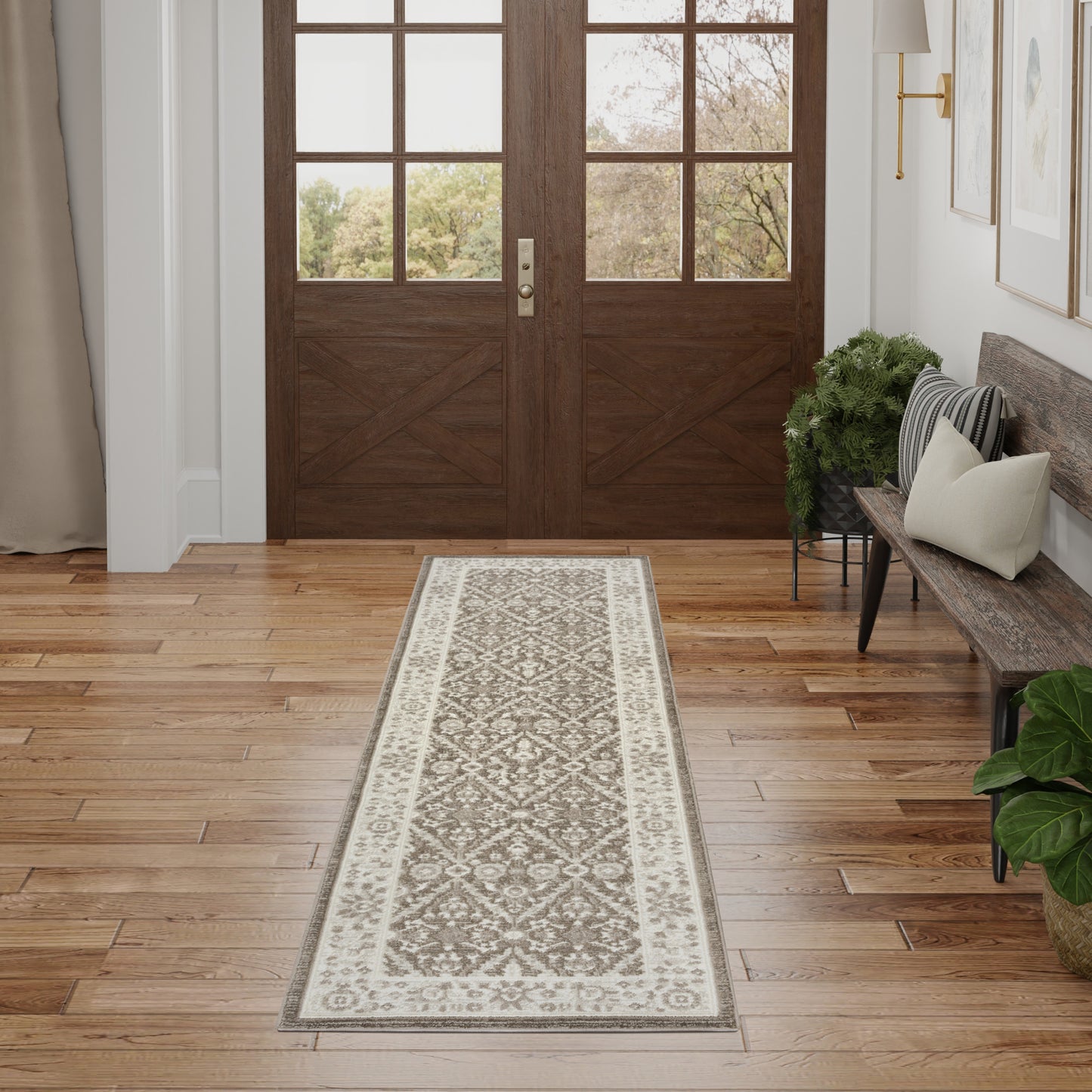 Grey & cream patterned runner rug in a wood-floored entryway with double doors, bench with pillows & plants.
