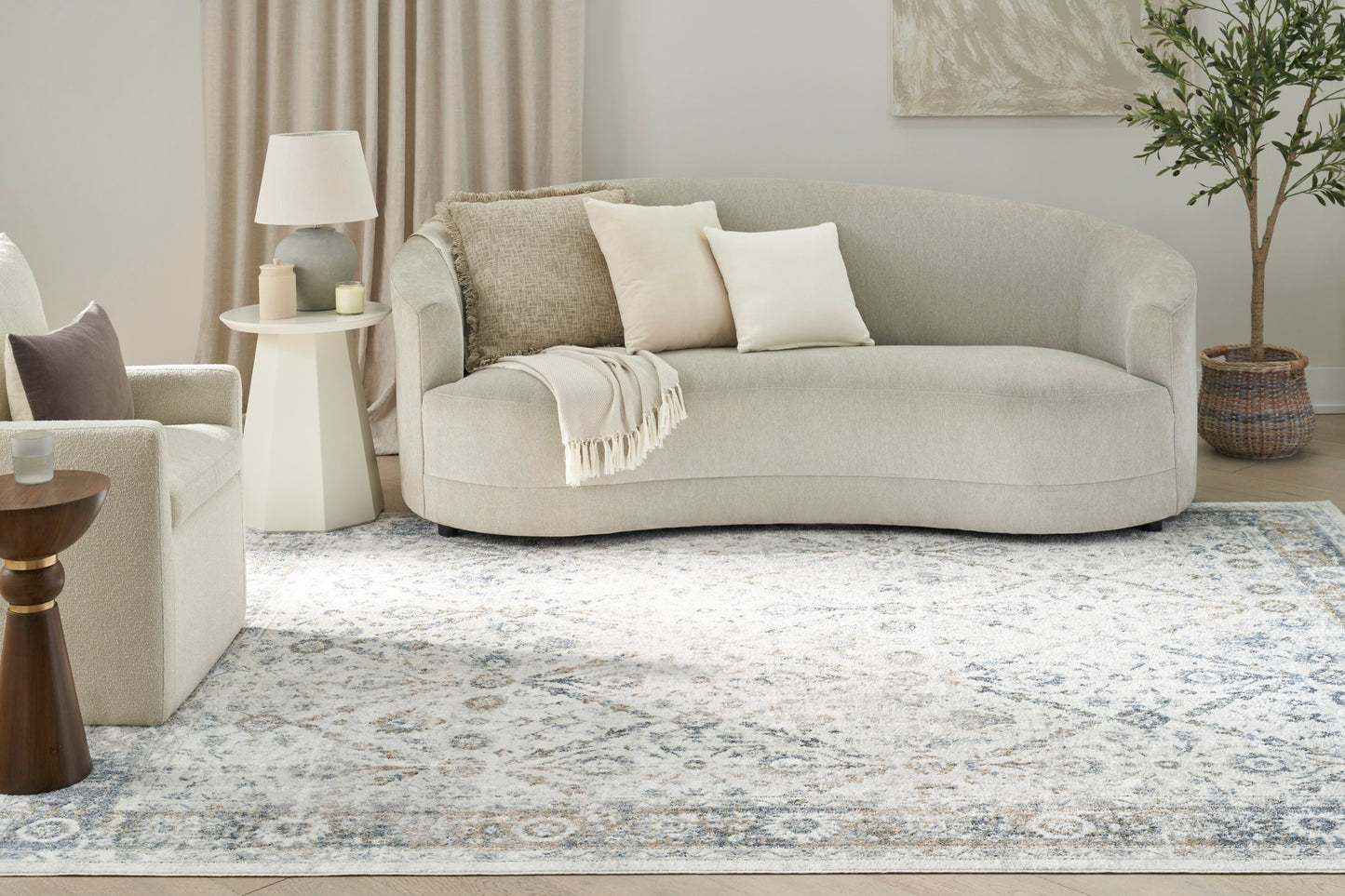 8' x 10' vintage rug with a cool-toned patterned design on a living room floor & a light beige curved sofa, a side table lamp, a plant & neutral decor nearby.