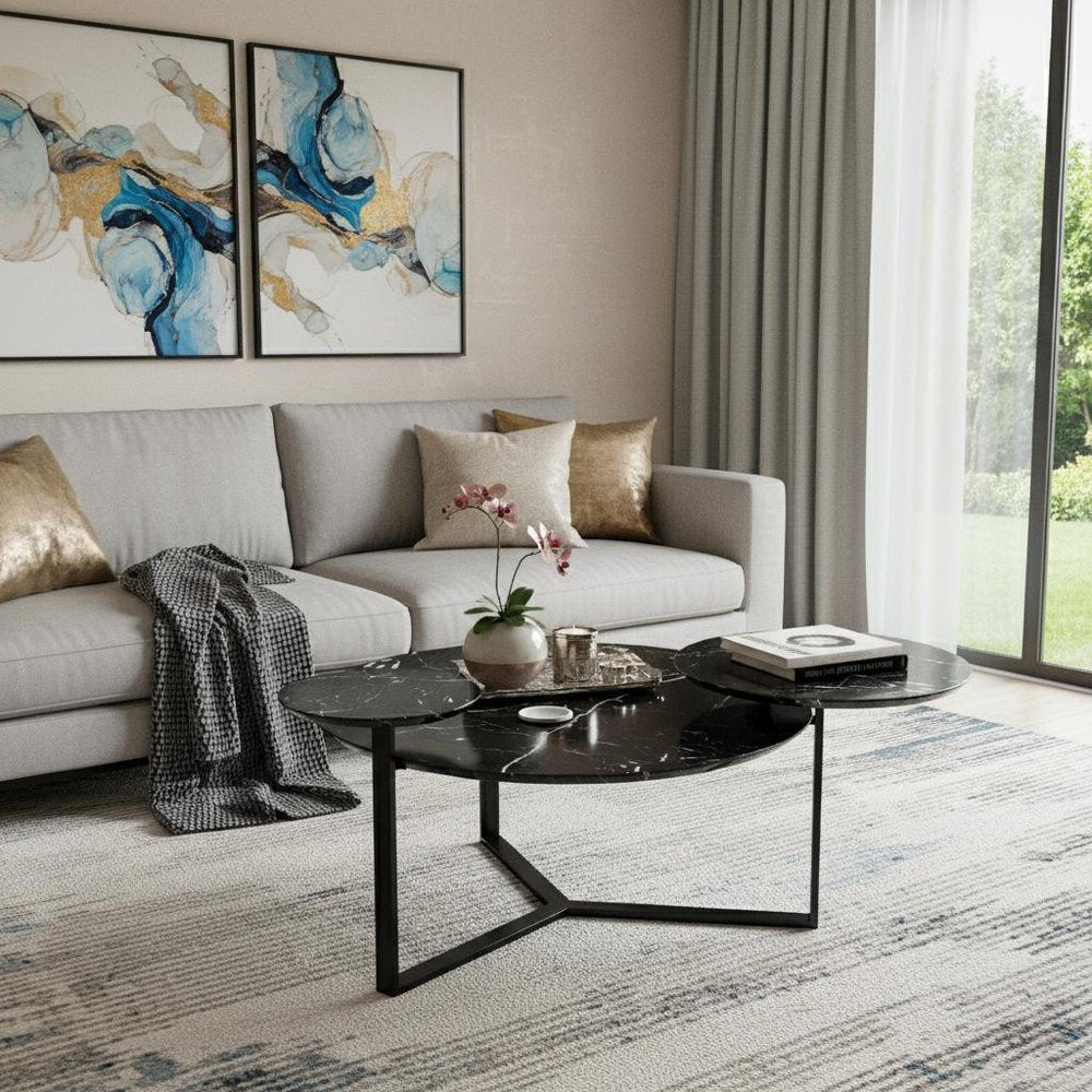 Modern living room with light gray sectional, gold cushions, black two-tier round coffee table, blue-gold abstract wall art, and large window with sheer curtains.