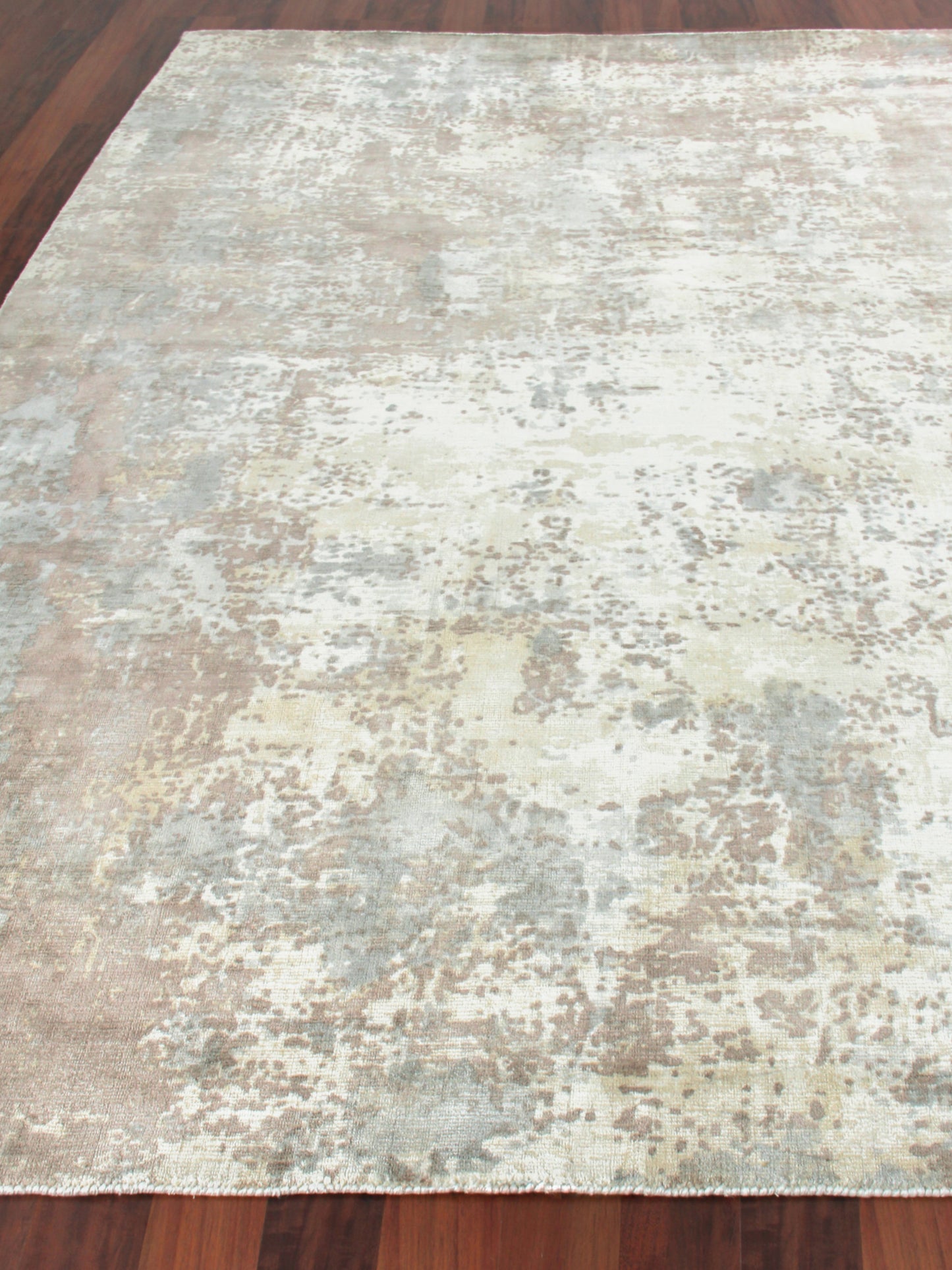 Rectangular distressed abstract area rug in cream, beige, gray and pale blue on dark hardwood floor.