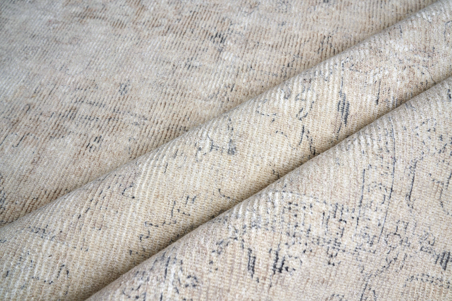 Beige woven rug with subtle blue-gray abstract pattern and soft tweed-like texture, folded.
