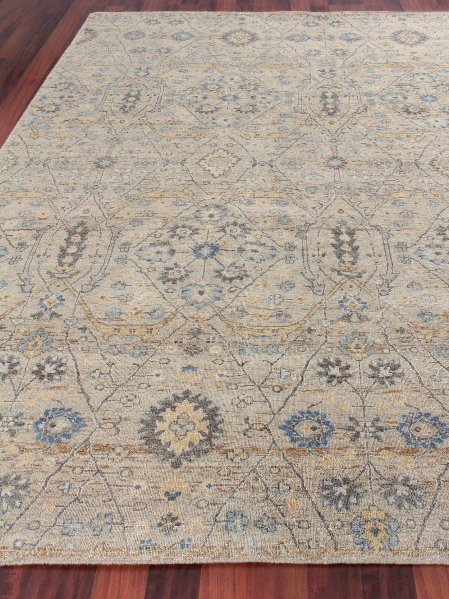 Beige area rug with blue and gray floral lattice pattern on hardwood floor.