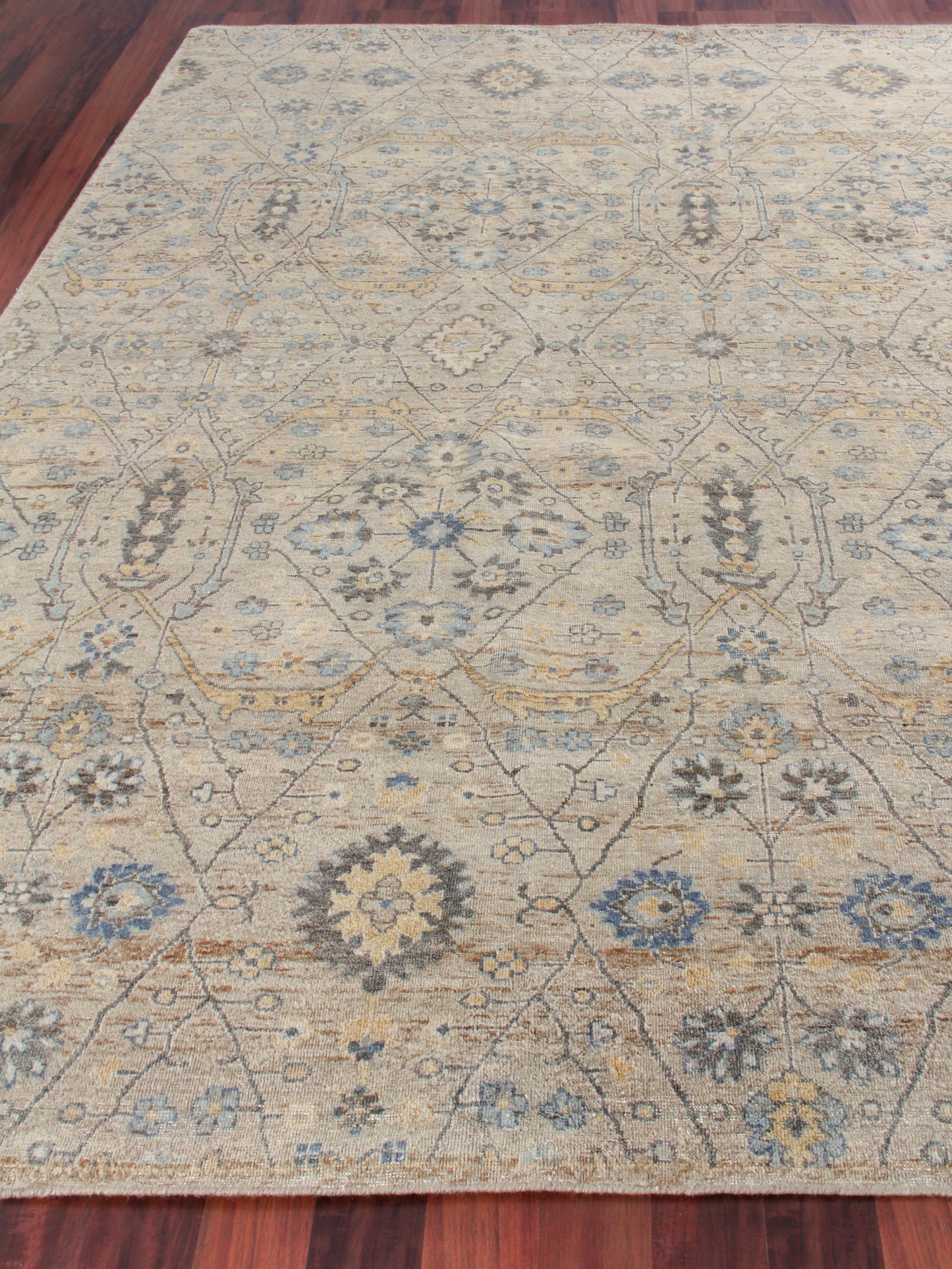 Beige oriental area rug with blue gray floral medallions and lattice motifs on a dark hardwood floor.