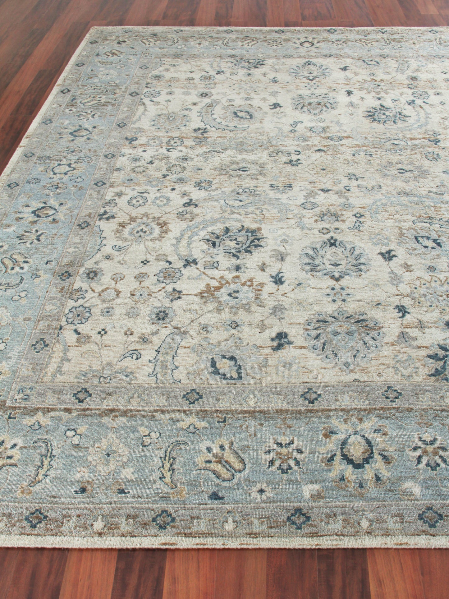Blue and ivory traditional rug with floral medallions and bordered edge on a wooden floor.