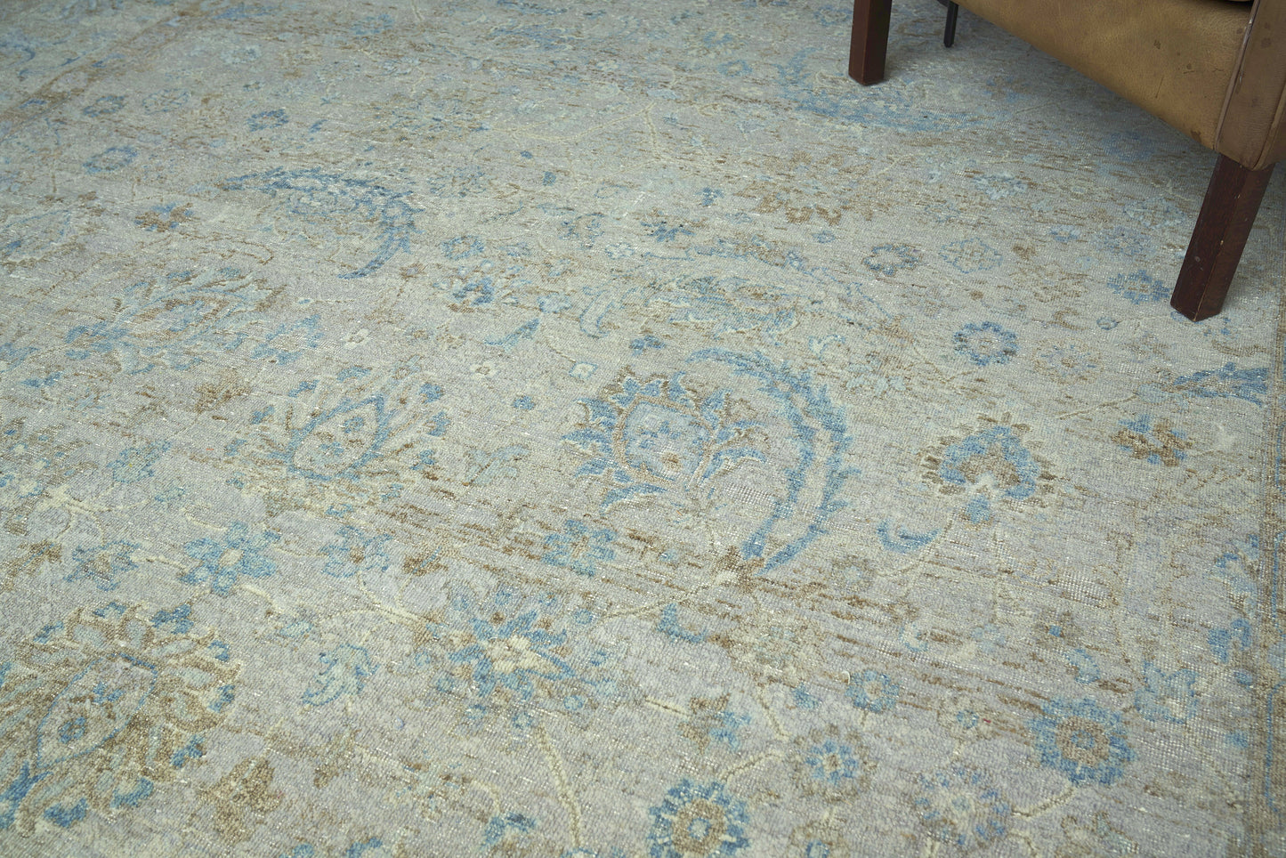 Blue and beige oriental rug with floral medallions, distressed vintage look; woven texture; sofa leg visible at corner.