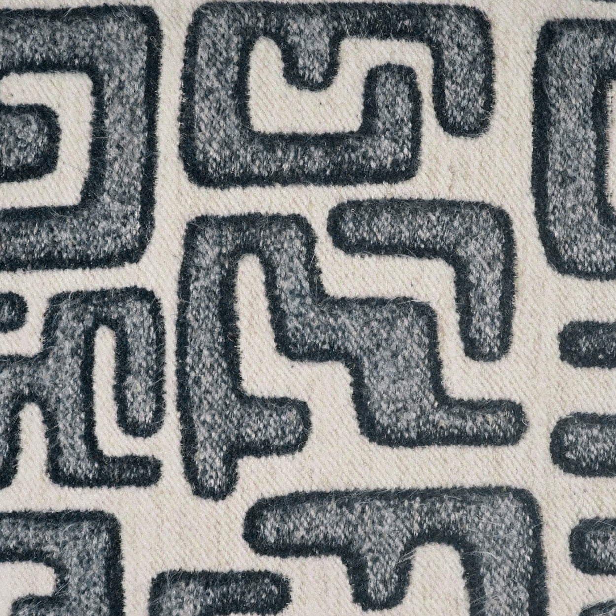 Close-up fabric with a dark gray interlocking geometric Greek-key pattern on cream background; plush textured nap.