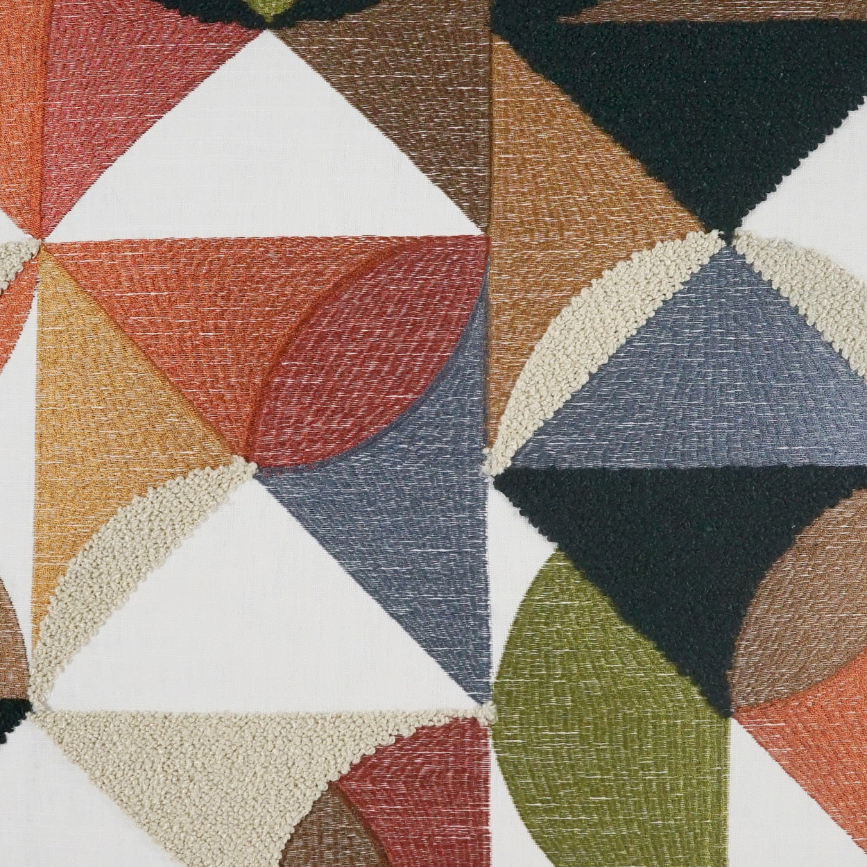 Geometric patchwork fabric with triangles and curved shapes in red, orange, blue, green; decorative woven upholstery textile.