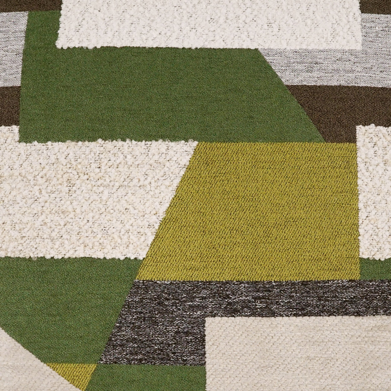 Geometric patchwork rug with olive green, mustard, cream and brown blocks in a textured weave.