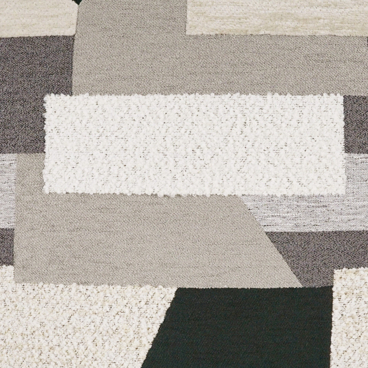 Geometric patchwork area rug in cream, beige, taupe, gray and black with varied shaggy plush textures.