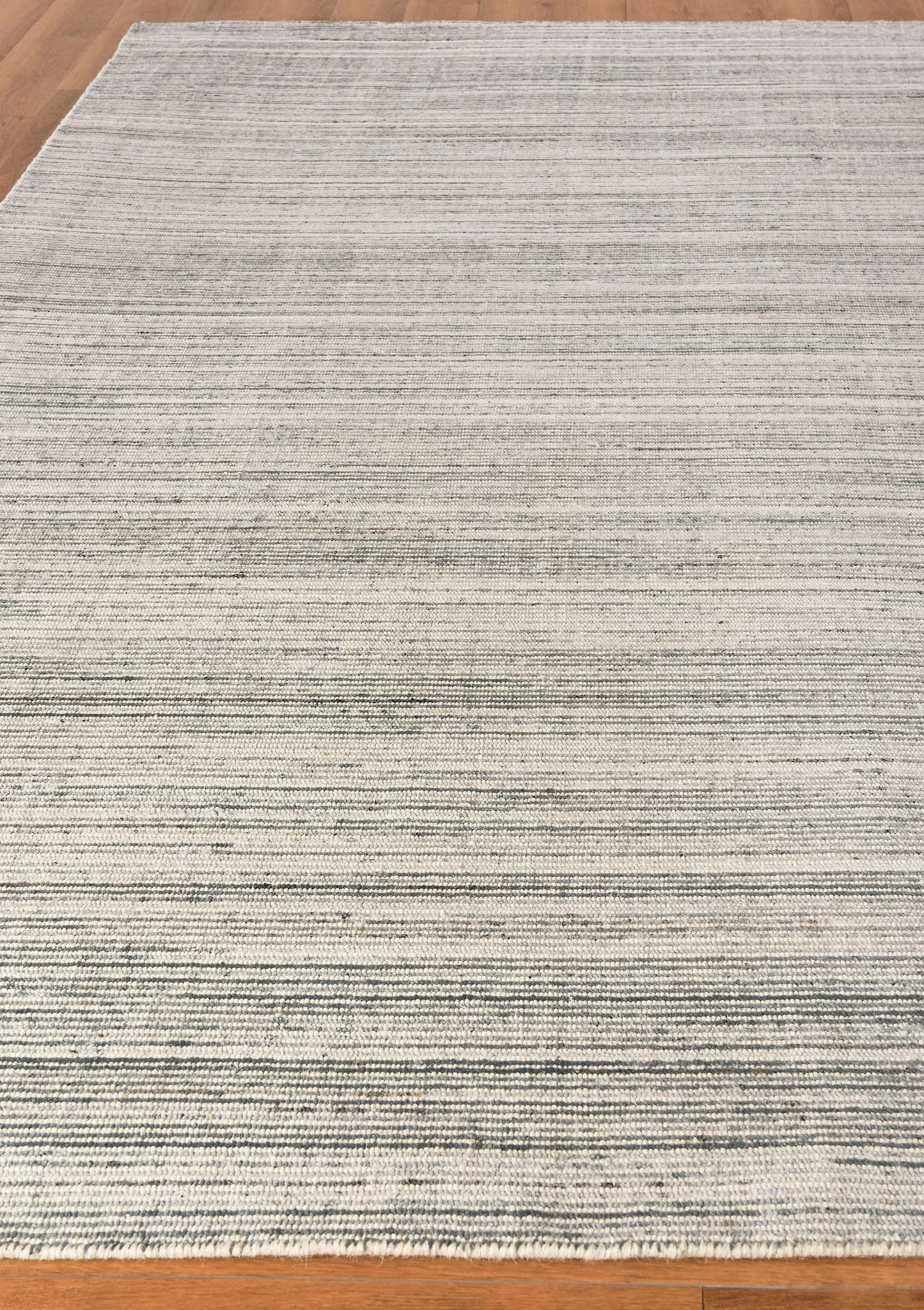 Light gray woven area rug with thin horizontal charcoal stripes and a fringed edge on a wooden floor.