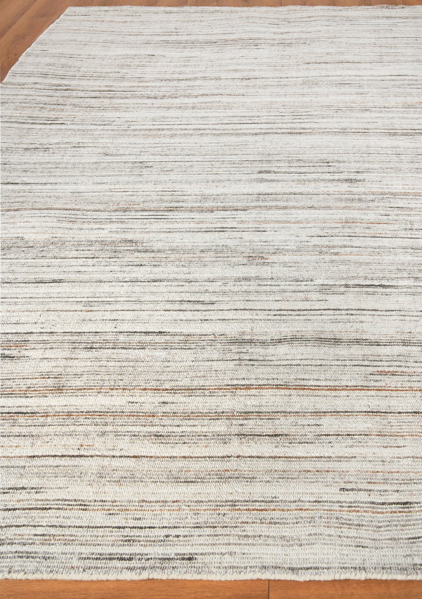 Light gray hand loomed rug with subtle dark stripes, rectangular, on a wooden floor.
