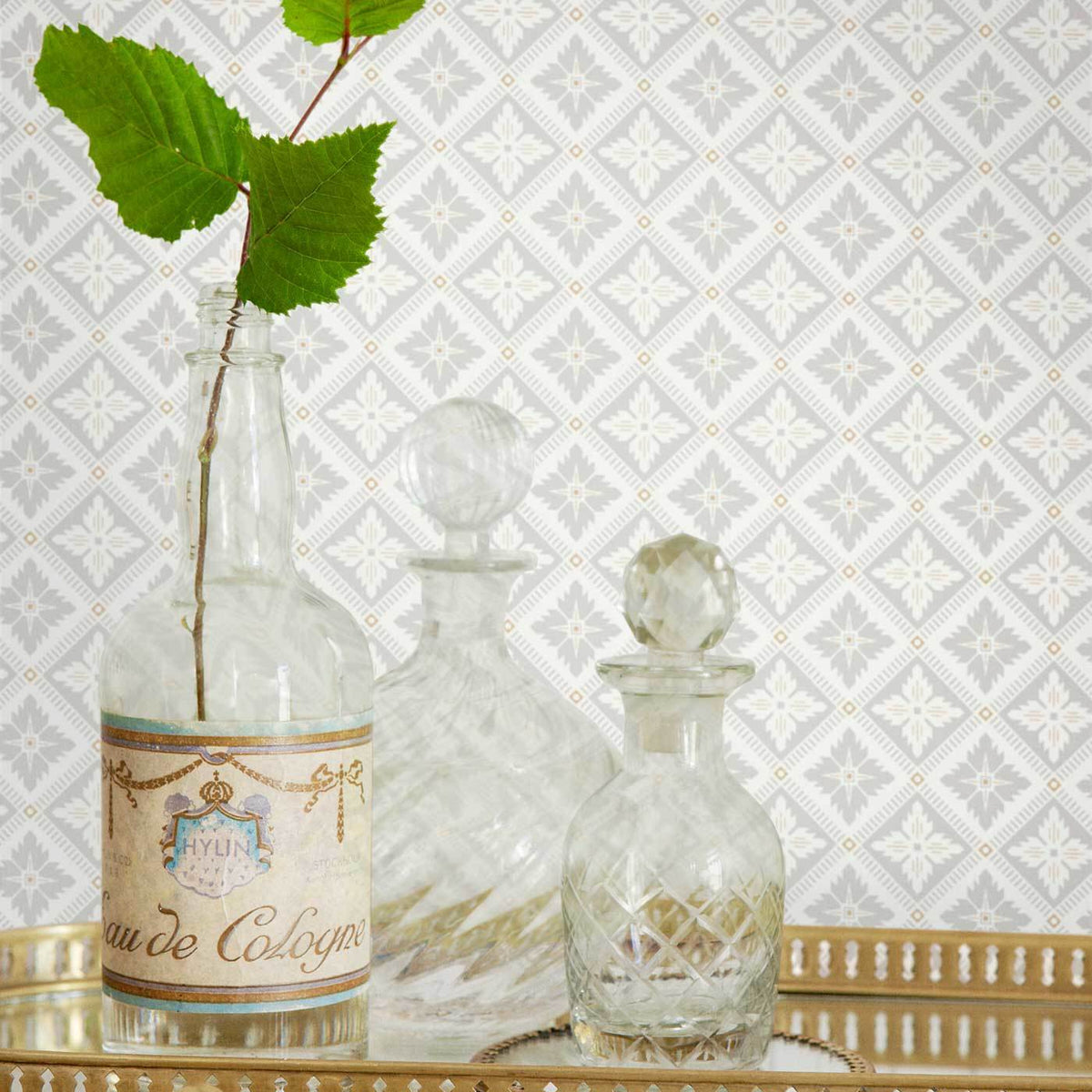 Vintage glass decanter set with cut-crystal bottles, one labeled Eau de Cologne, greenery in a bottle, on a gold tray.