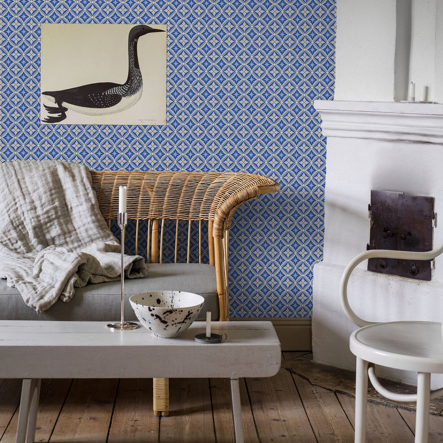 Cozy living room with blue geometric wallpaper, gray sofa with throw, white coffee table, ceramic bowl, candles, white chair, and fireplace