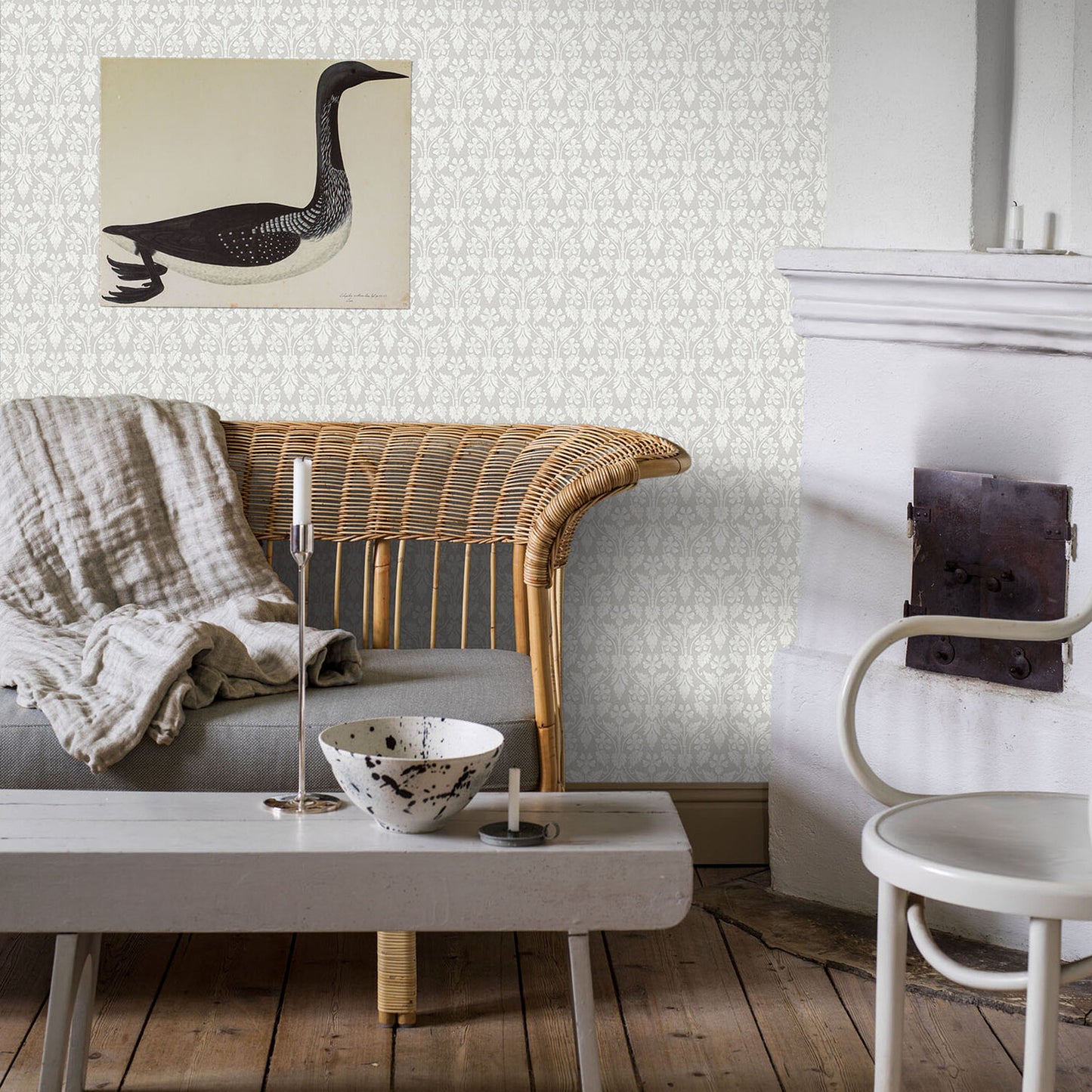 Living room with gray damask wallpaper, wicker sofa, linen throw, white coffee table, speckled bowl, candle, duck wall art.