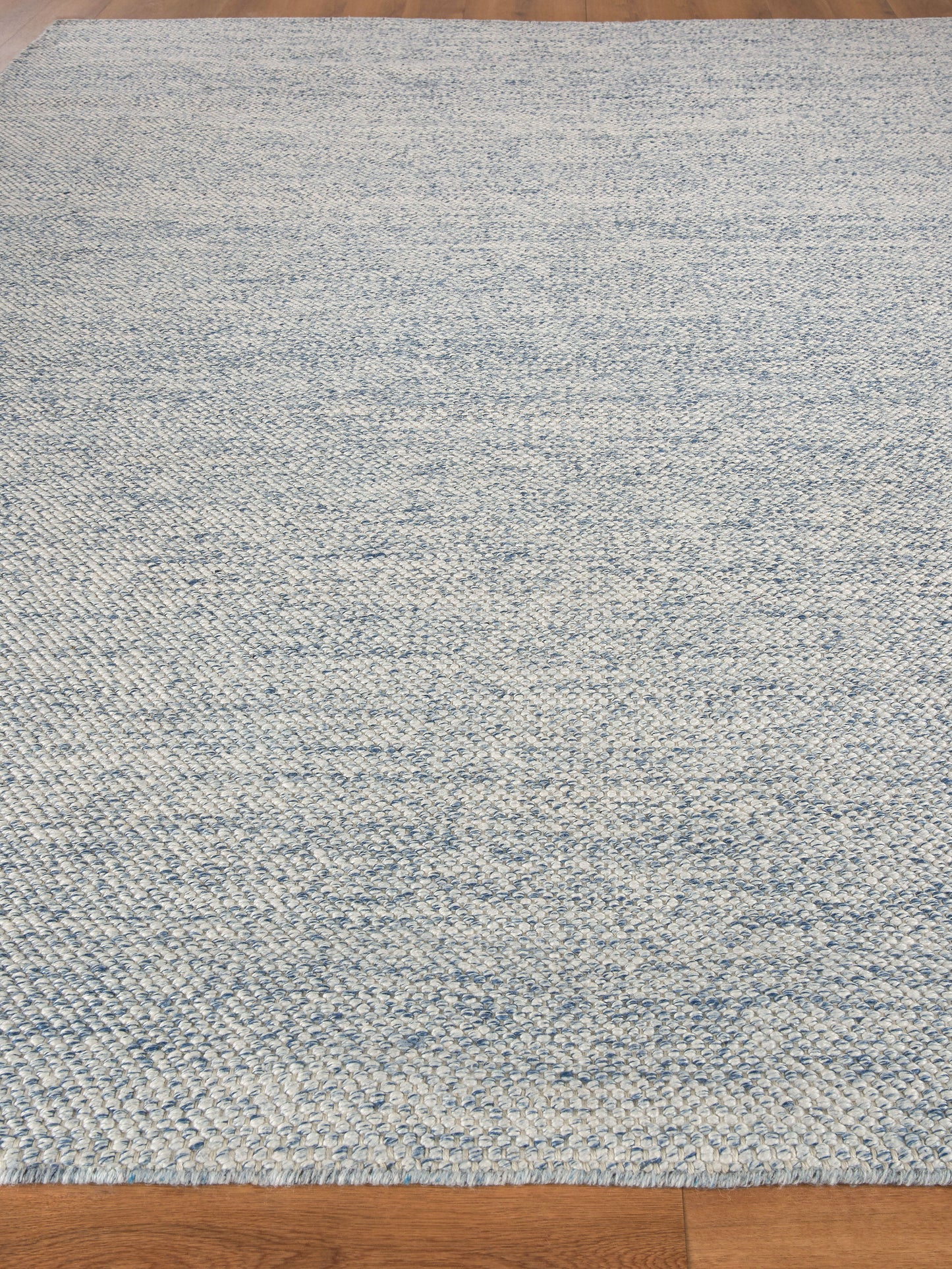 Rectangular blue and ivory marled hand loomed rug on hardwood floor.
