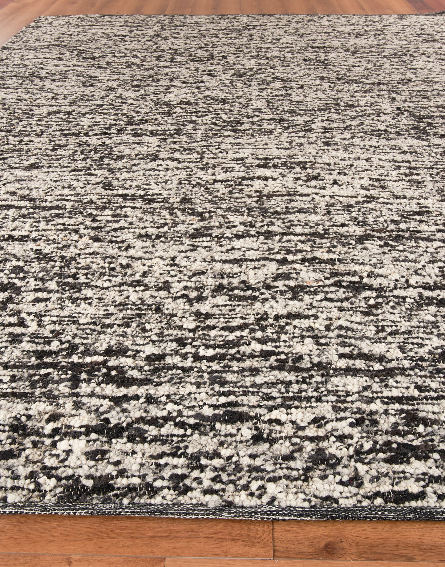 Rectangular area rug with black, gray and ivory speckled distressed pattern on a wooden floor.