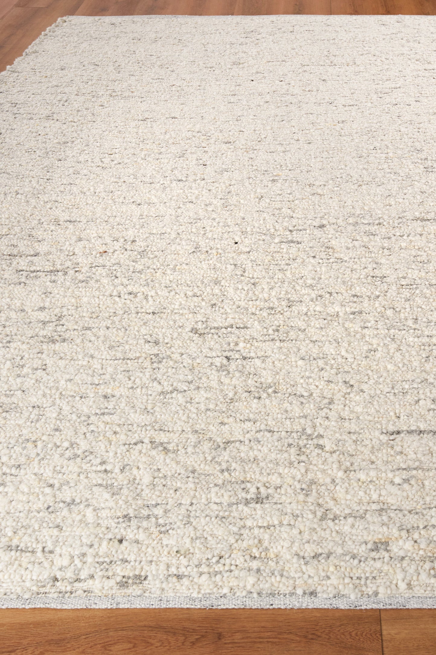 Cream textured area rug with subtle gray speckling on wood floor; rectangular flat-weave rug.
