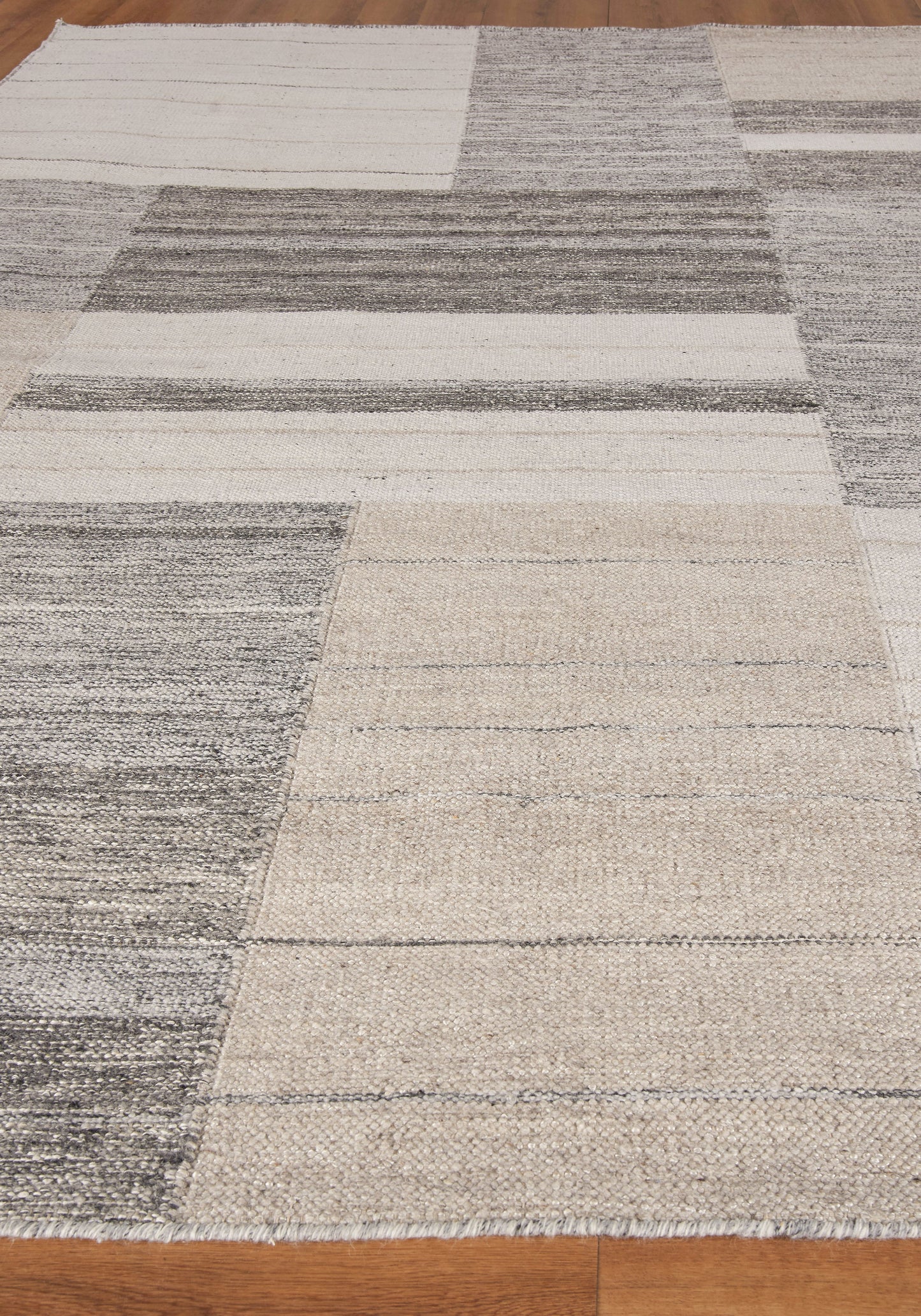 Neutral patchwork area rug in beige, cream and gray, woven texture with fringe edges.