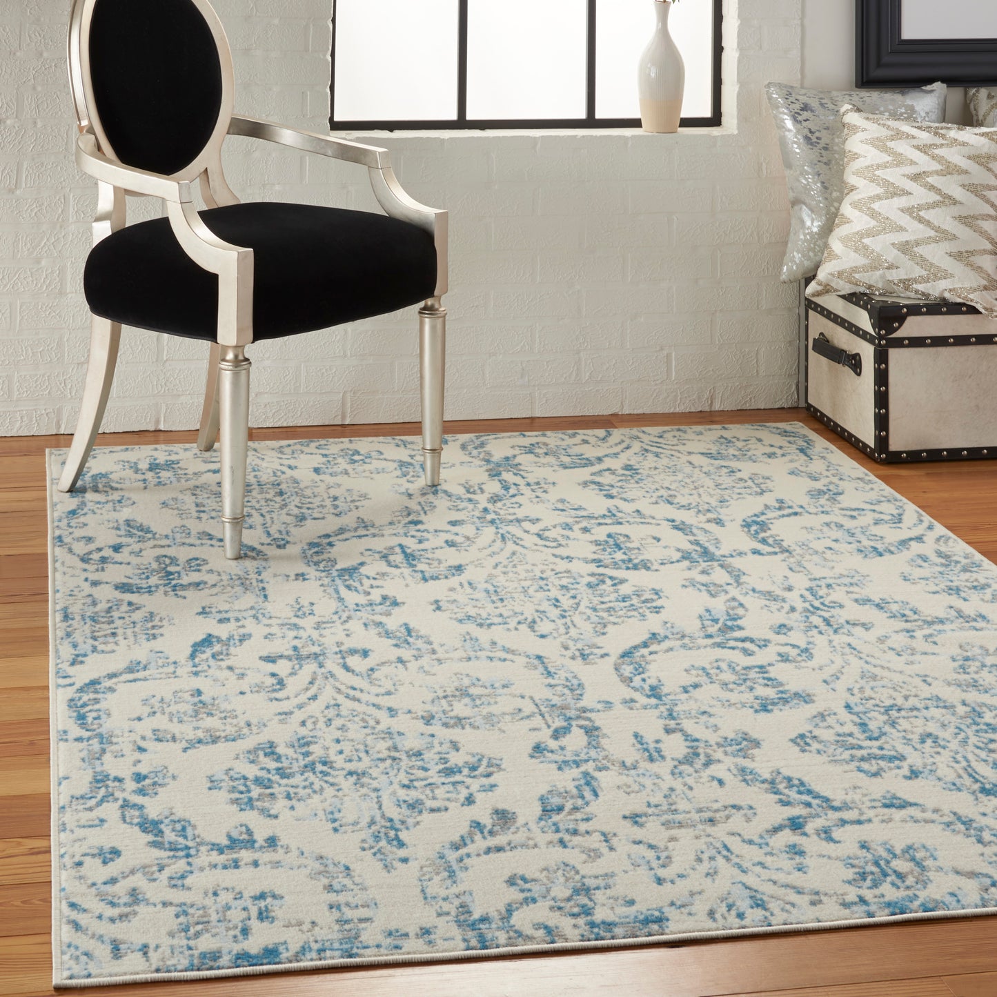 Cream and blue damask area rug under a vintage white carved chair with black cushion in a bright room.