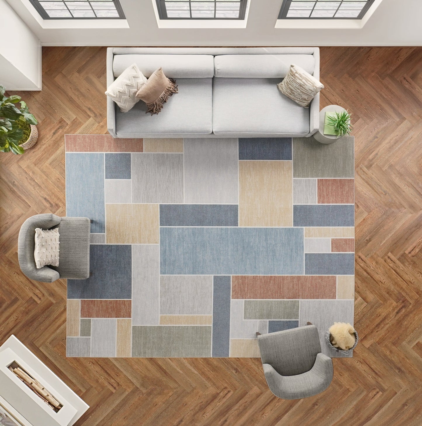 Top-down view of living room with a geometric patchwork area rug in blues, beiges, and browns on herringbone wood floor; light gray sofa and chairs.