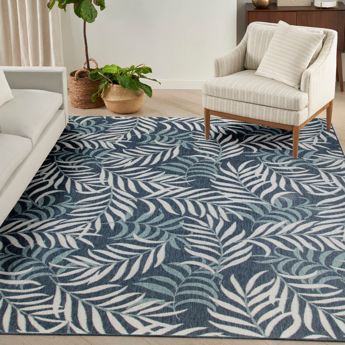 Navy blue area rug with white palm-leaf pattern in a neutral living room with beige fabric sofa and striped armchair.