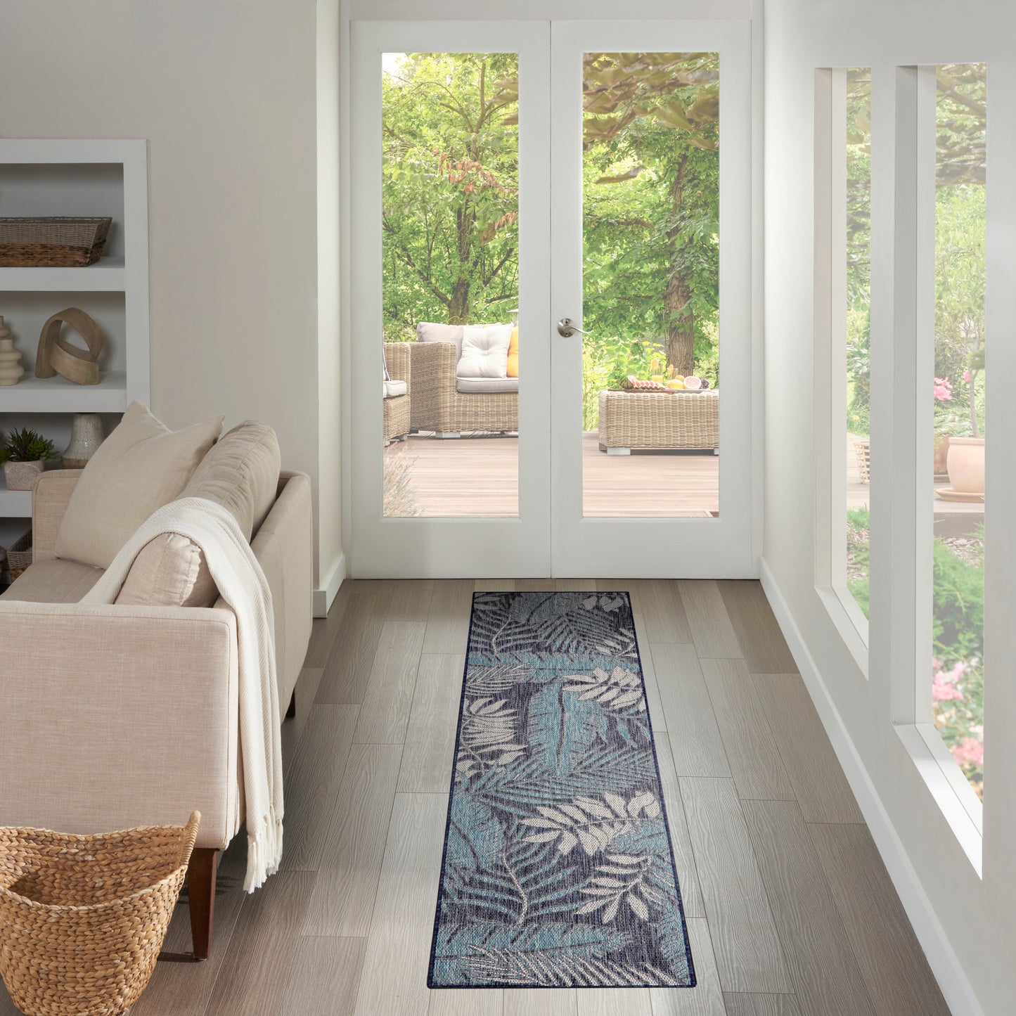 Teal botanical runner rug in a light wood hallway toward white-framed French doors, with beige sofa and wicker basket.