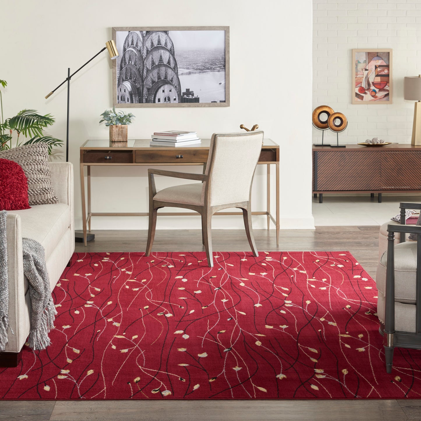 Red patterned area rug with ivory leaf motifs under a beige upholstered wooden desk chair in a modern living room.